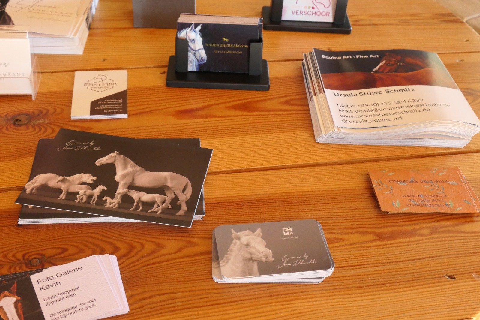 Business cards and brochures on a wooden table, featuring images of horses and related artwork.