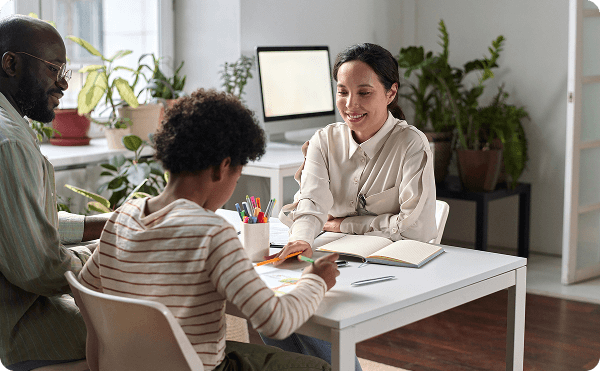 Psychologist collaborates with a child and parent at a table, reviewing drawings and notes in a calm, supportive office.