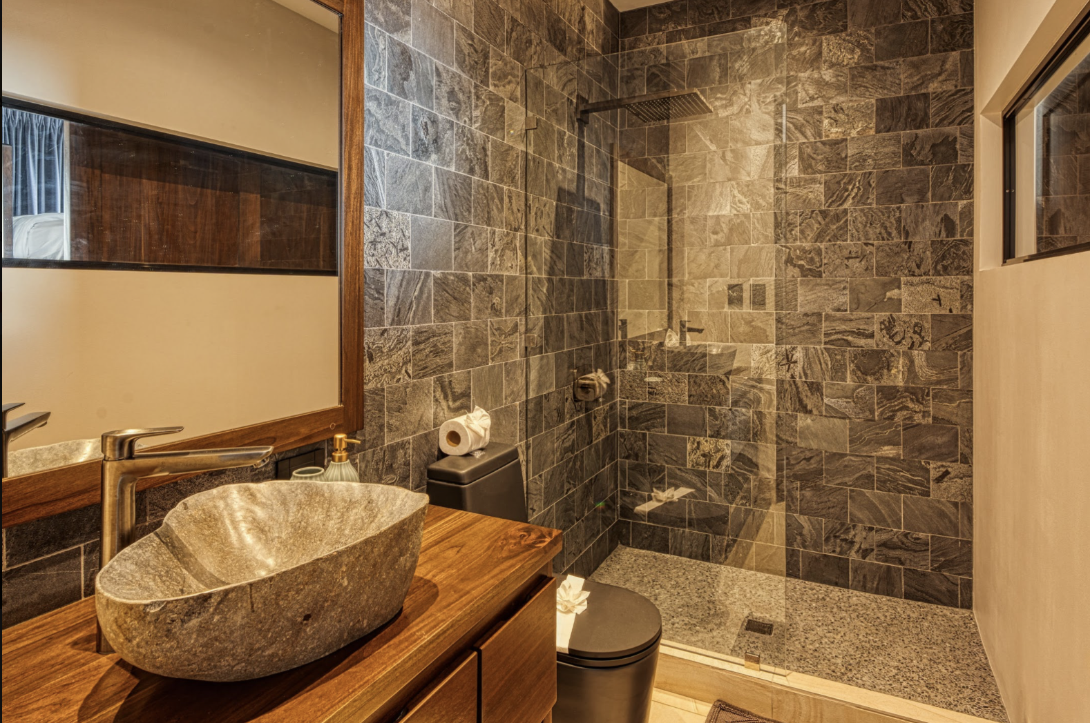 Modern bathroom featuring a stone vessel sink, wooden countertop, large mirror, and a walk-in shower with tiled walls and a glass door.