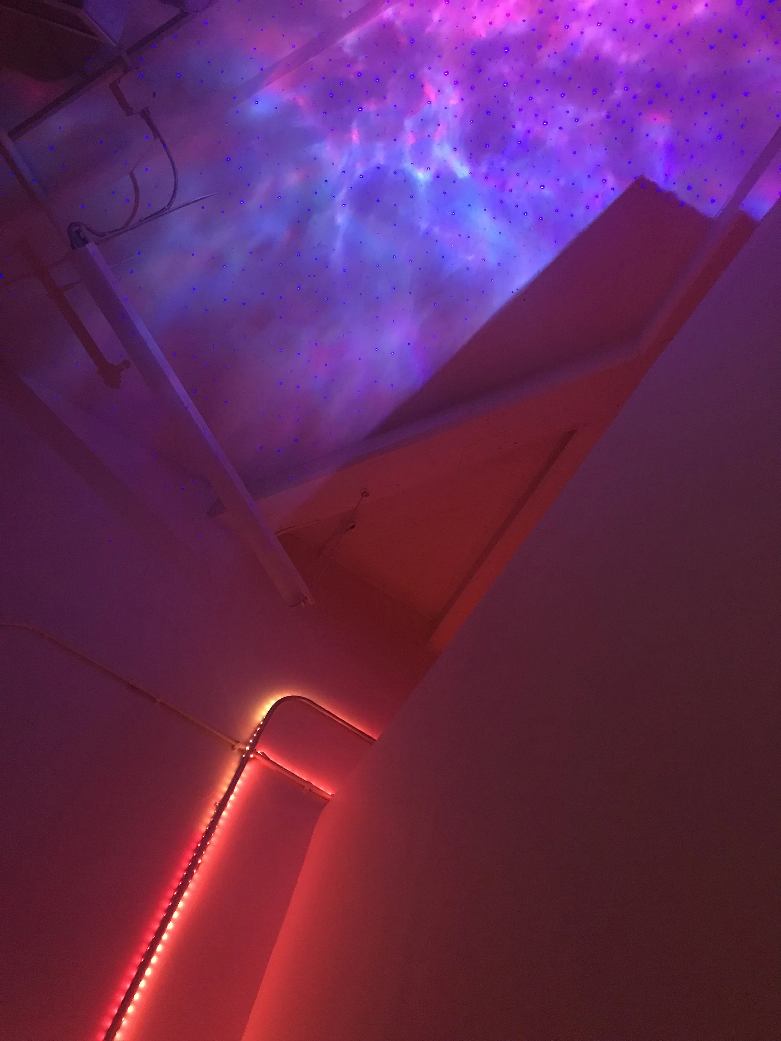 nebulous magents and purple lighting on celing of Thai massage Vermont studio. A warm glowing orange light lines the wall