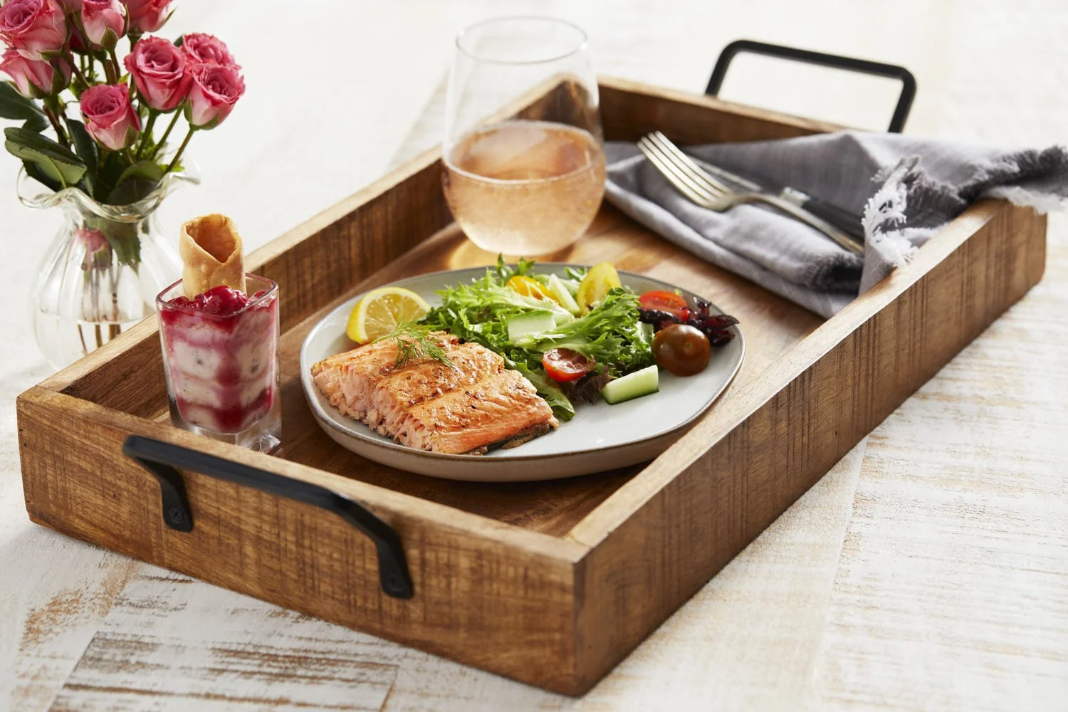 Plate with a piece of grilled salmon and a salad on a wood serving tray with a mini dessert and a glass of rose wine. Soft window lighting. Created by Seattle based food photographer Mike Gluckman.