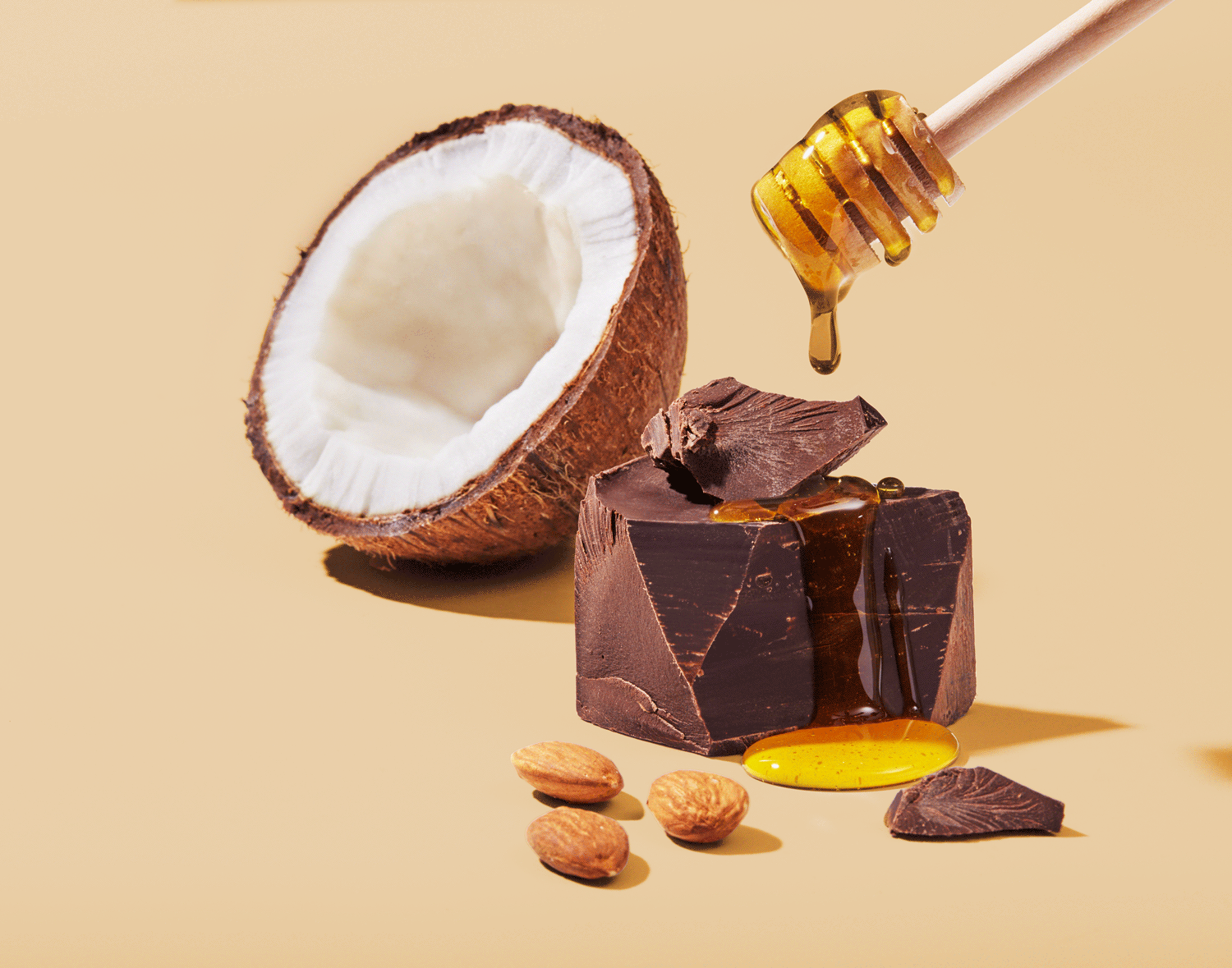 A coconut half, large chunk of dark chocolate and almonds with honey dripping from a honey wand. Packaging shot by Seattle CPG photographer Mike Gluckman.