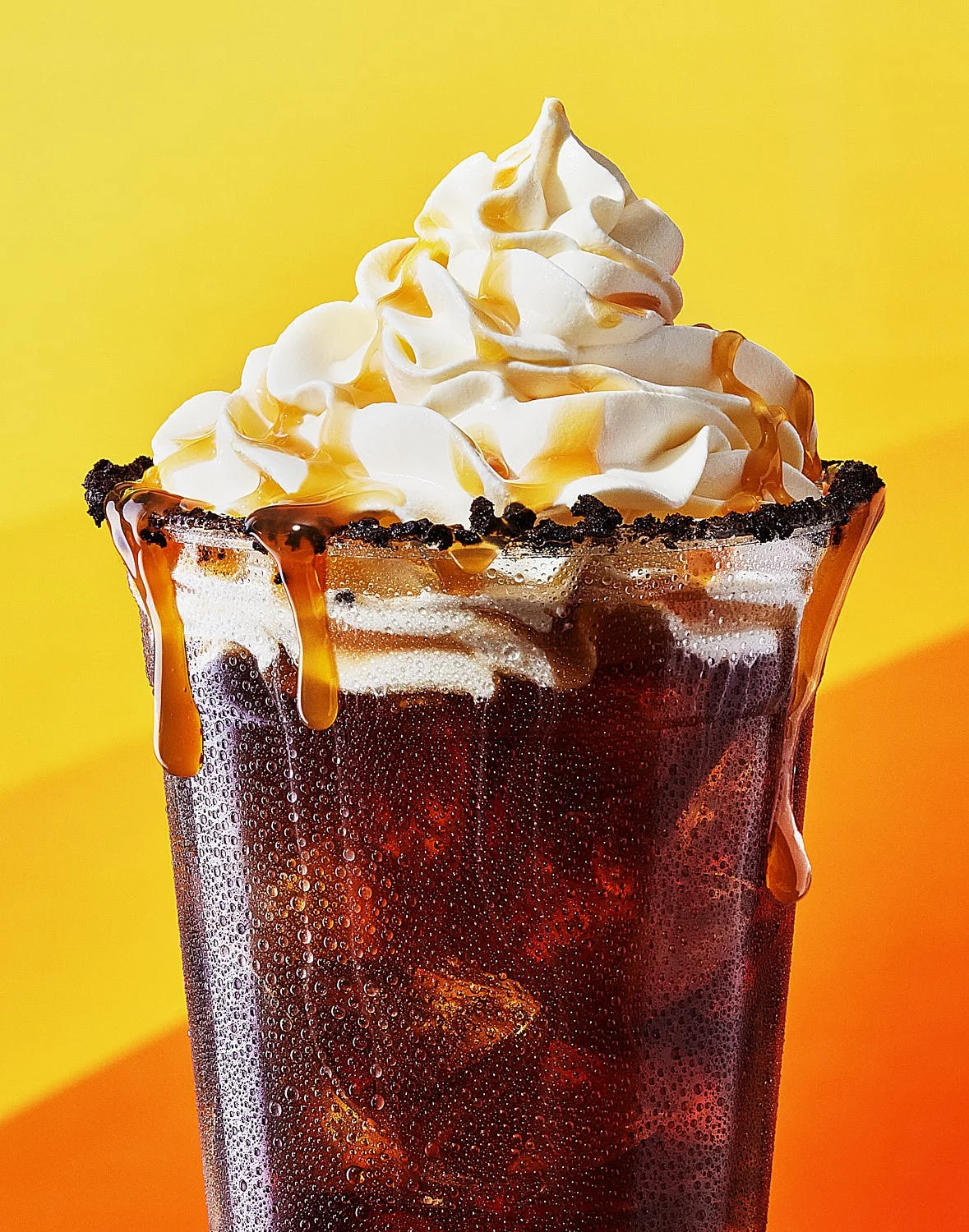 Starbucks style iced coffee in clear plastic to go cup with chocolate cookie crumbs, whipped cream and caramel sauce dripping down the side. Created by Seattle beverage video director and photographer Mike Gluckman.