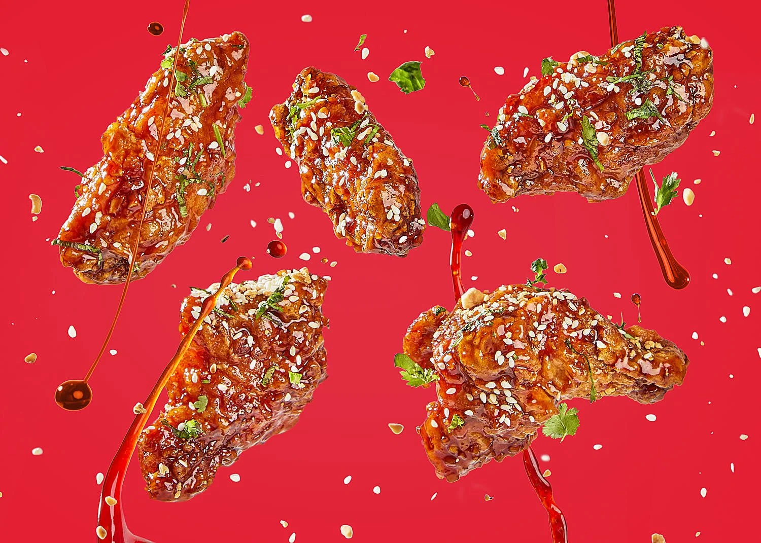 Five Korean twice-fried chicken (KFC) wings tossed in the air with sauce, cilantro, sesame seed, green onions and spices on a red background. Vibrant and bold monochromatic feel. CPG - consumer packaged goods photography by Seattle based food photogr