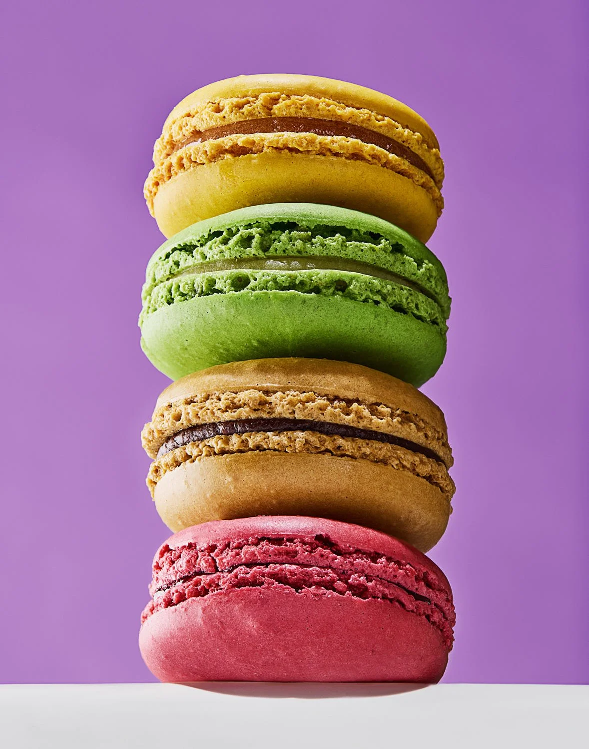 A stack of 4 colorful macaron pastries on a purple background. Bright lighting. Style is very clean and colorful. Seattle studio food photography by Mike Gluckman.