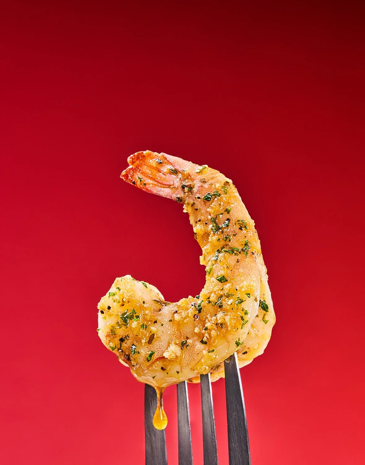 Close up of an Old Bay seasoned shrimp with butter drip on a fork. Red Background. Seattle food photography by Mike Gluckman