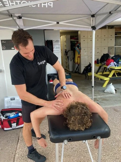 A Physiotherapist giving a back massage to someone lying on a massage table under a canopy at an outdoor setting.