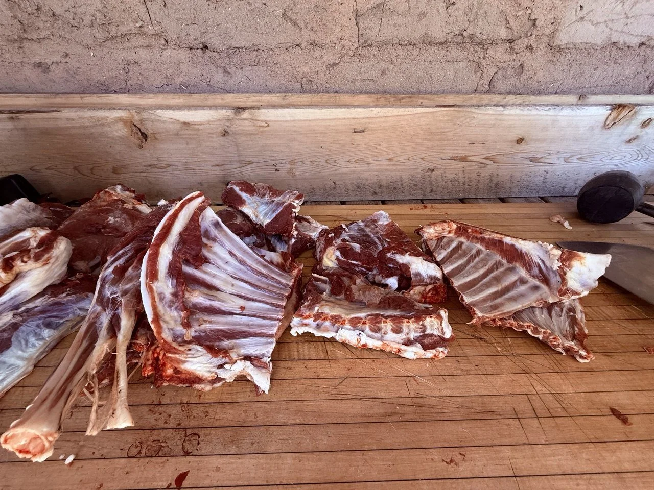 Various pieces of raw meat, including rack of ribs, on a wooden cutting board in a rustic kitchen setting.