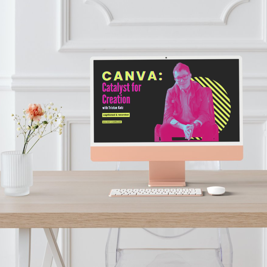 A computer monitor displaying a Canva workshop titled "CANVA: Catalyst for Creation" with Tristan Katz, featuring a pink silhouette of a smiling man sitting on a chair, on a black and yellow background. The monitor is on a light wooden desk with a white keyboard and mouse, and a small vase of flowers with pink and white blooms to the left.