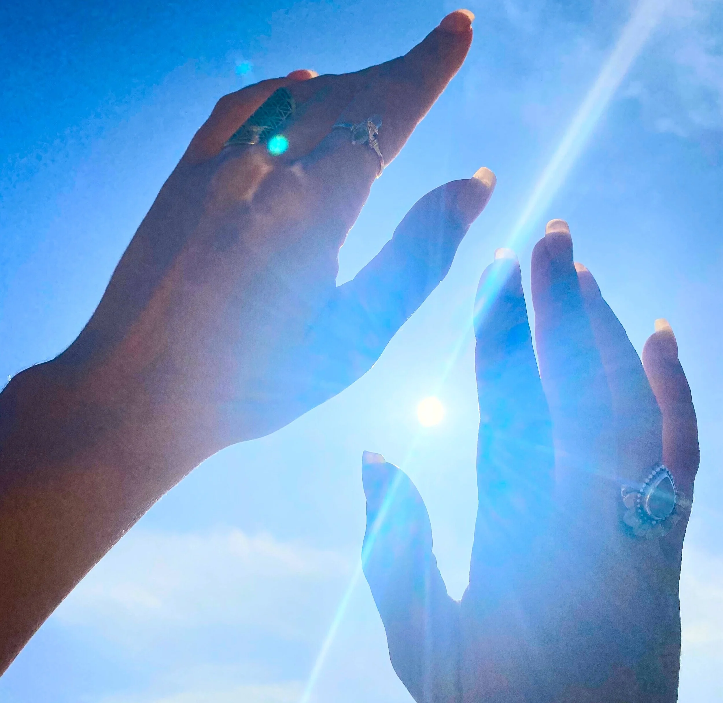 A hand reaching towards the bright sun in a clear blue sky with some slightly out-of-focus fingers at the bottom.