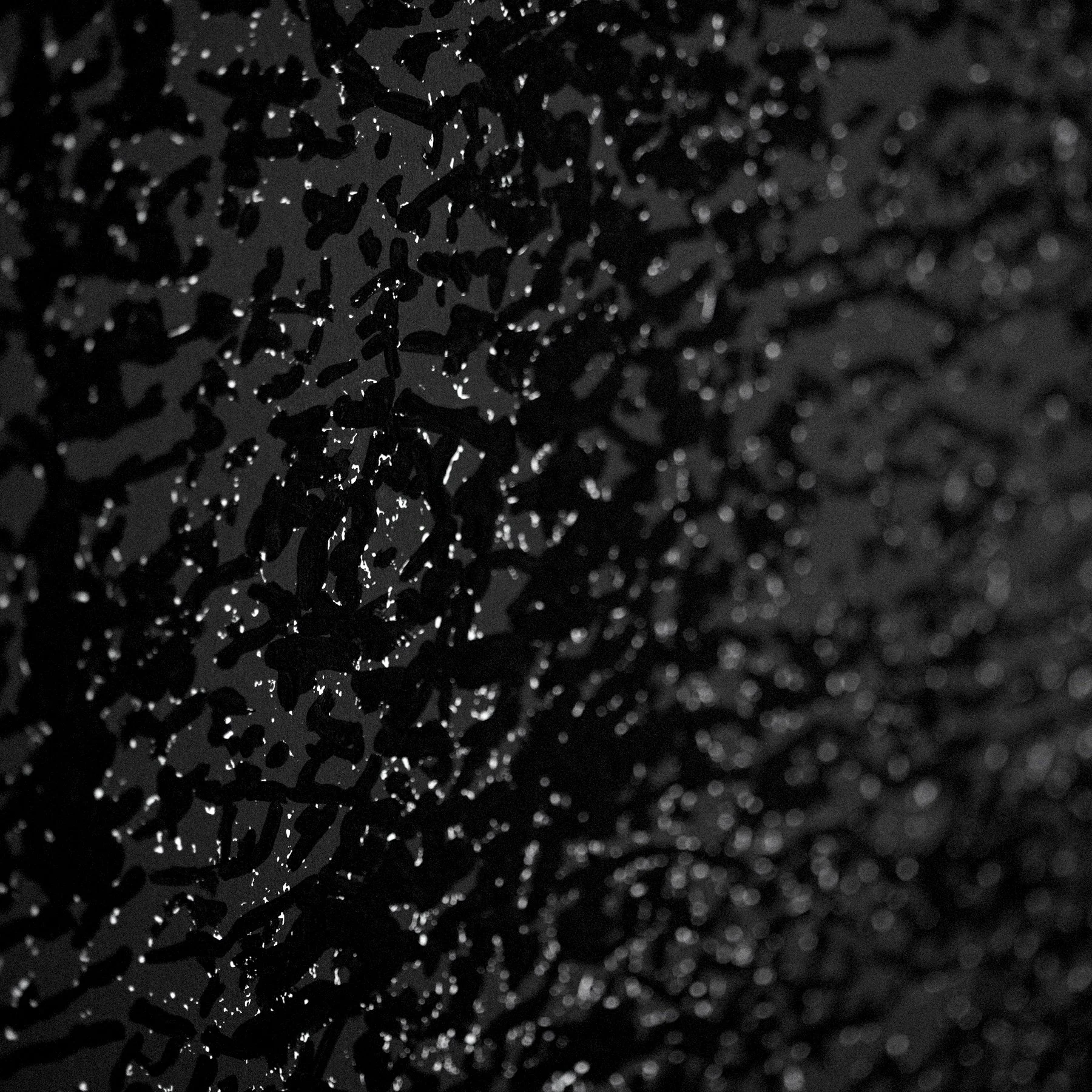 Close-up of water droplets on a dark, textured surface with high contrast lighting.