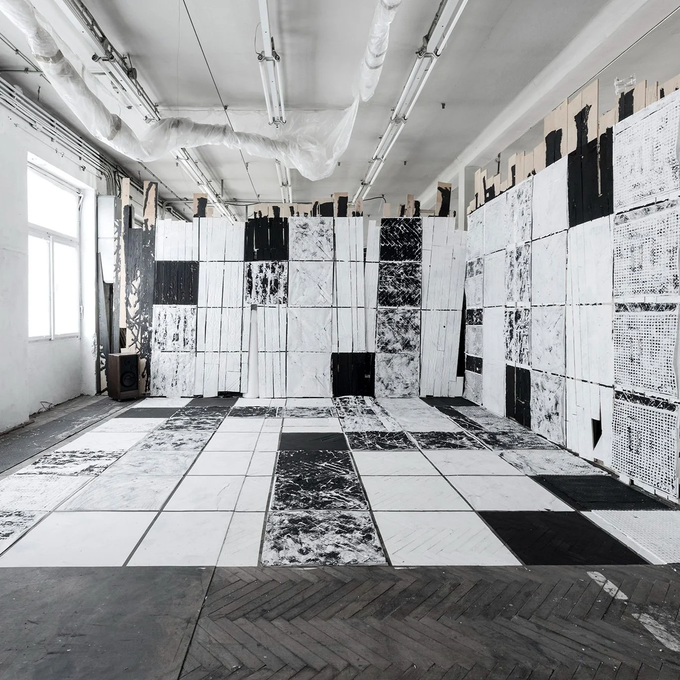 An art installation with large panels of marble or stone in black and white patterns arranged on the wall and floor, inside a room with natural light coming through windows.