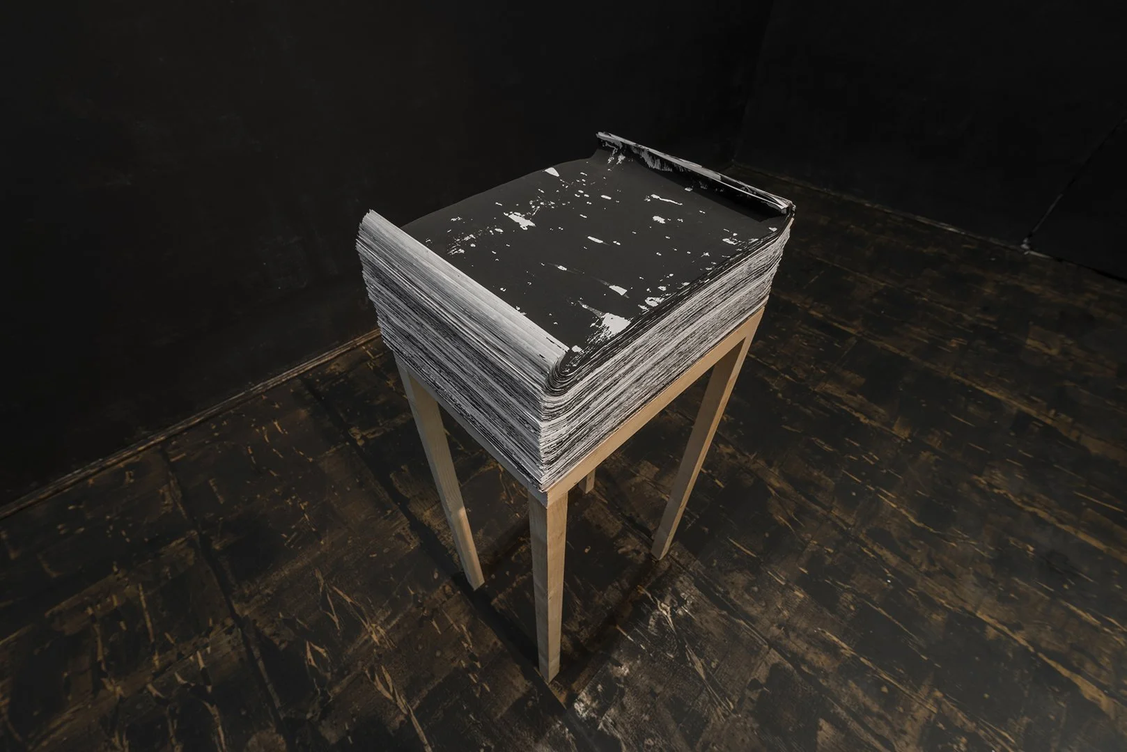 Close-up of print stack on wooden pedestal in dark conceptual installation by Gábor Koós