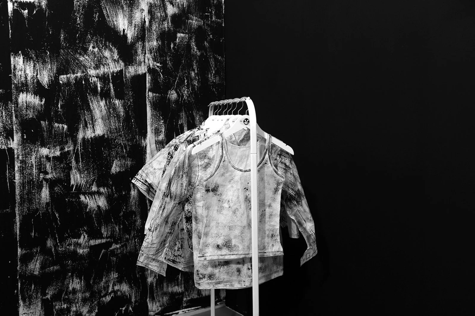 Shirts suspended on a minimalist rack within Gábor Koós’s immersive black-and-white installation environment.