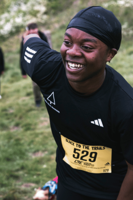a young person wearing a 'black to the trails' race number and smiling