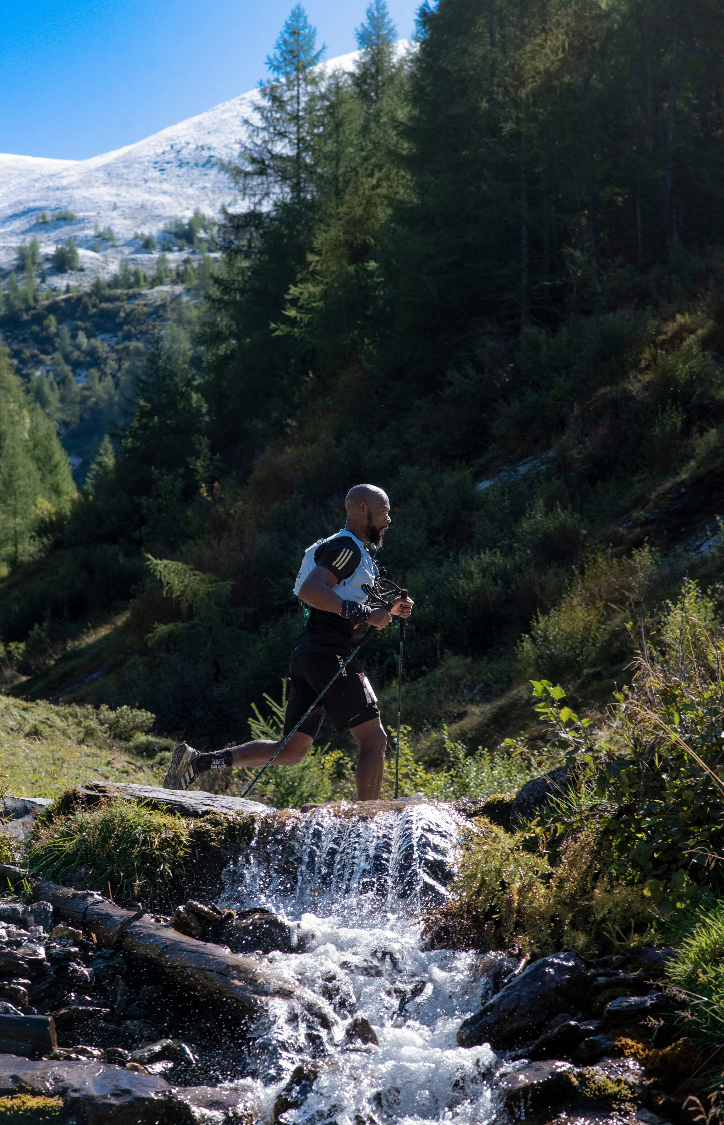 A man trail running with poles across a brook