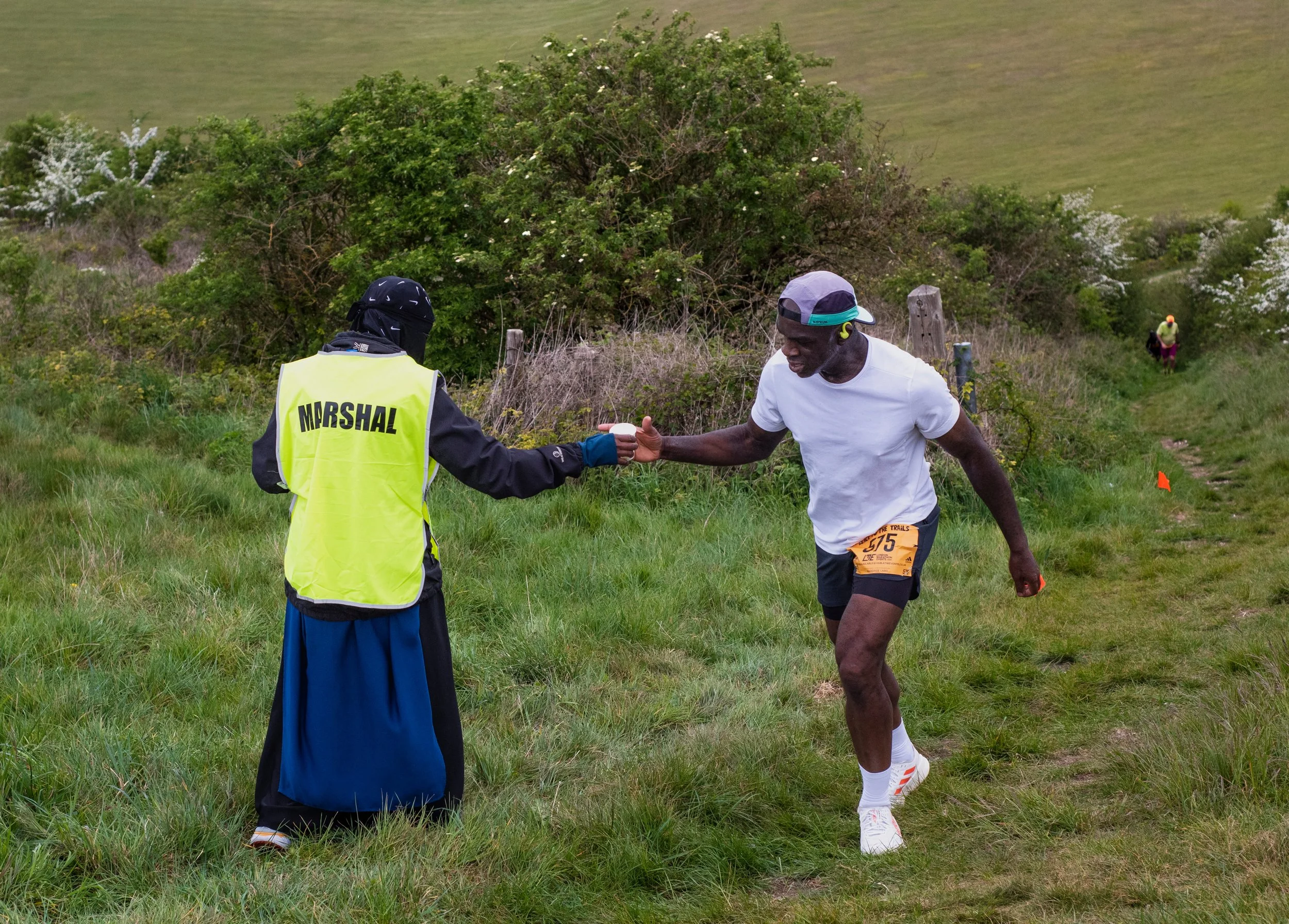 A race marshal handing a trail runner a cup of water