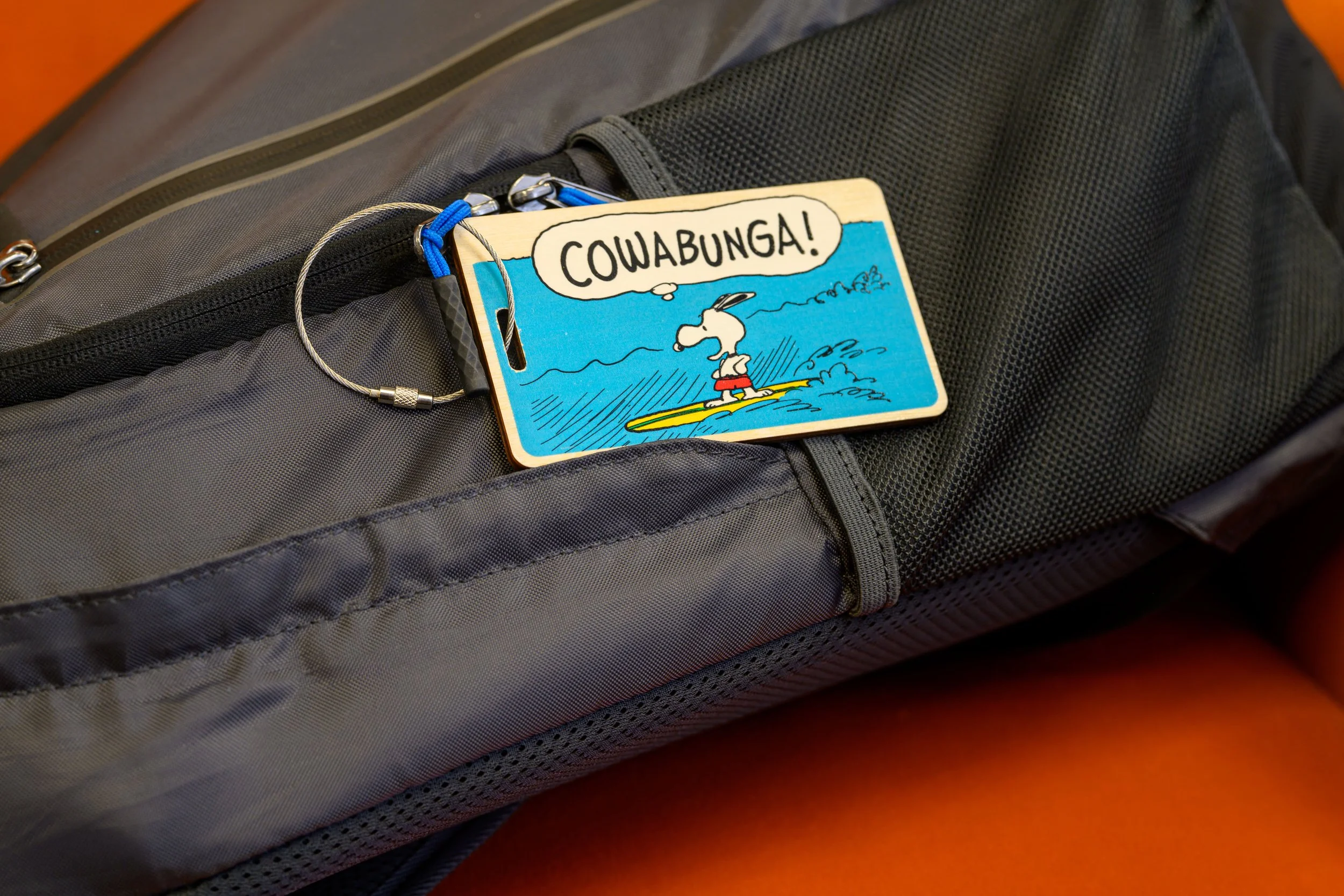 Ride the wave in style with this bold and playful Peanuts “Cowabunga” Wooden Bag Tag featuring Snoopy on a surfboard ready to take on the ocean! This colorful and durable tag measures 2.65" x 4.5", and is crafted from premium wood, making it a stando