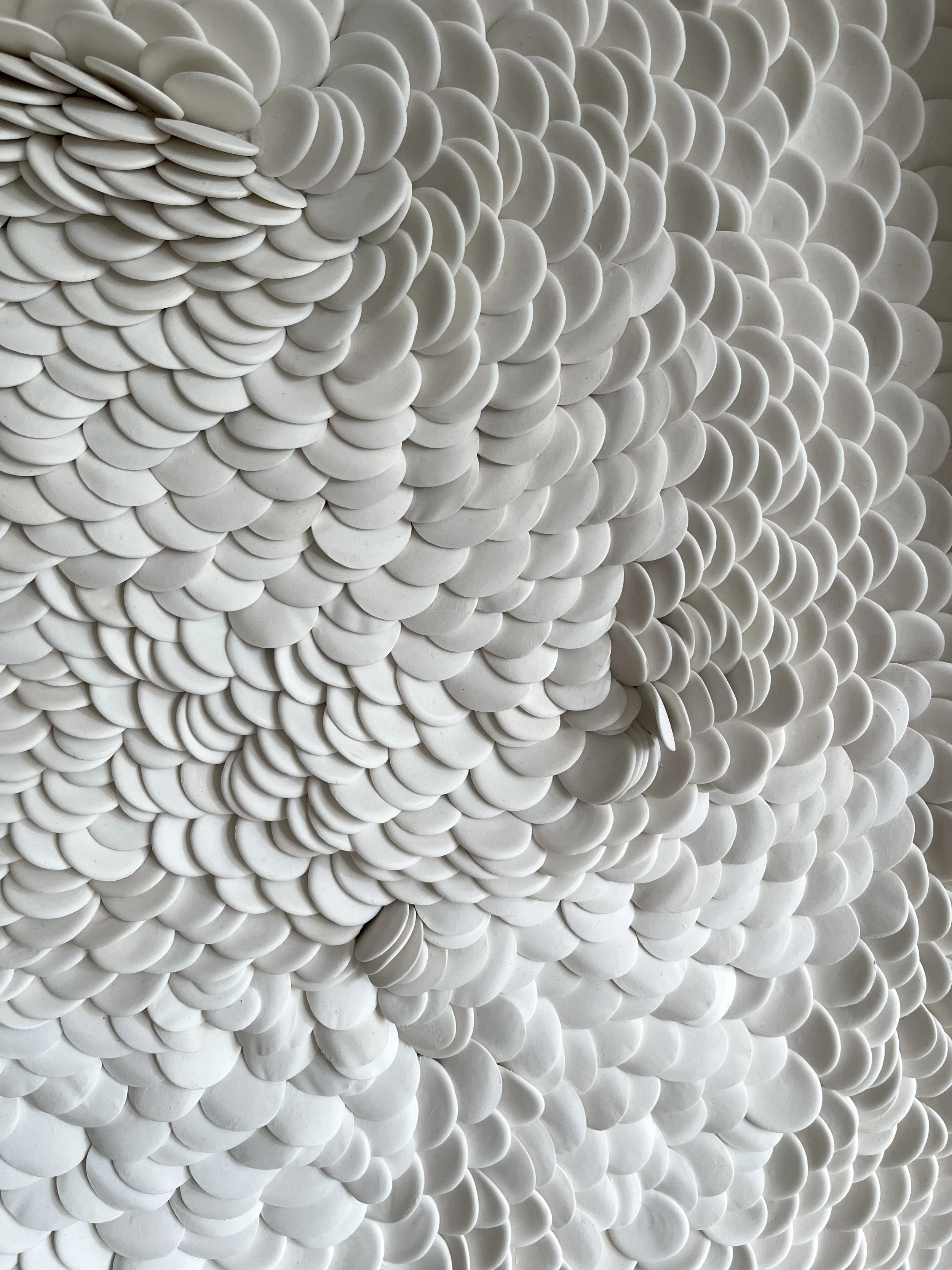 Side perspective of a white porcelain wall sculpture showing flowing contours and subtle variations in surface relief.
