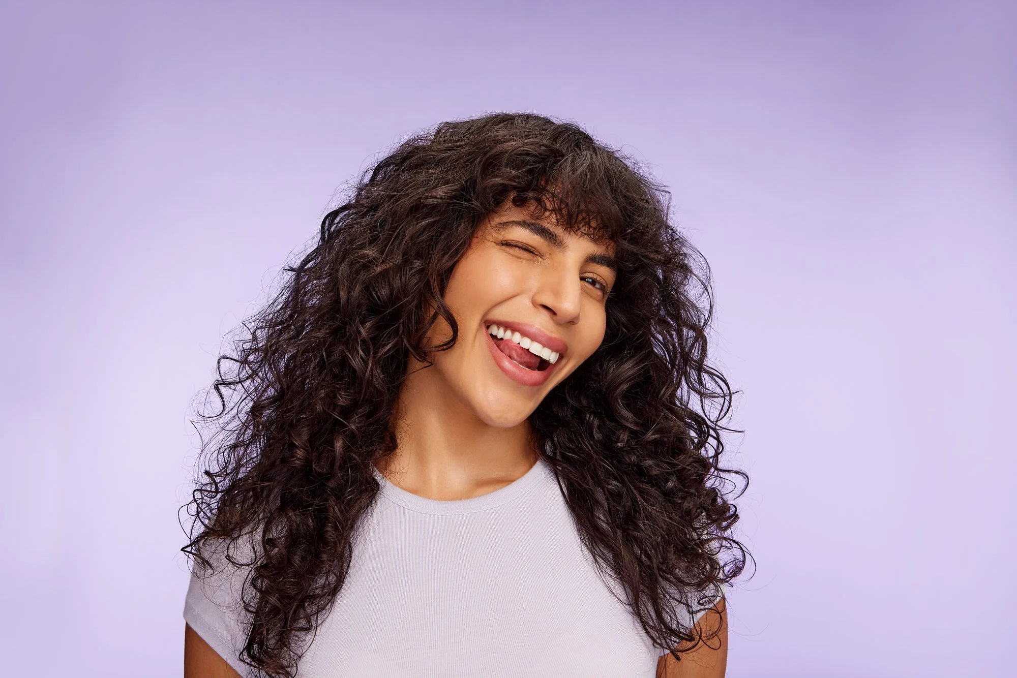 Model with dark curly hair swishing her hair in colourful Noughty Haircare campaign shoot