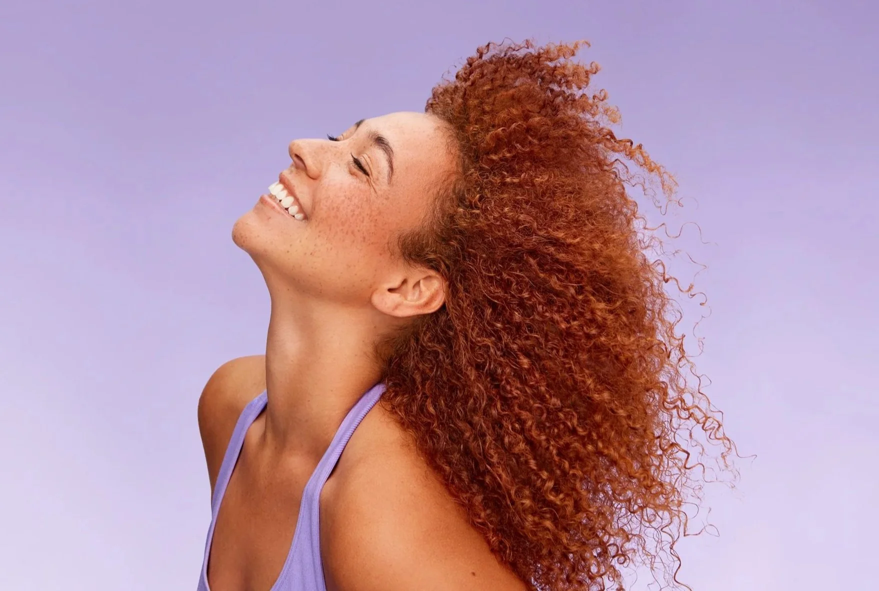 Model with tightly coiled red afro hair swishing her hair in colourful Noughty Haircare campaign shoot
