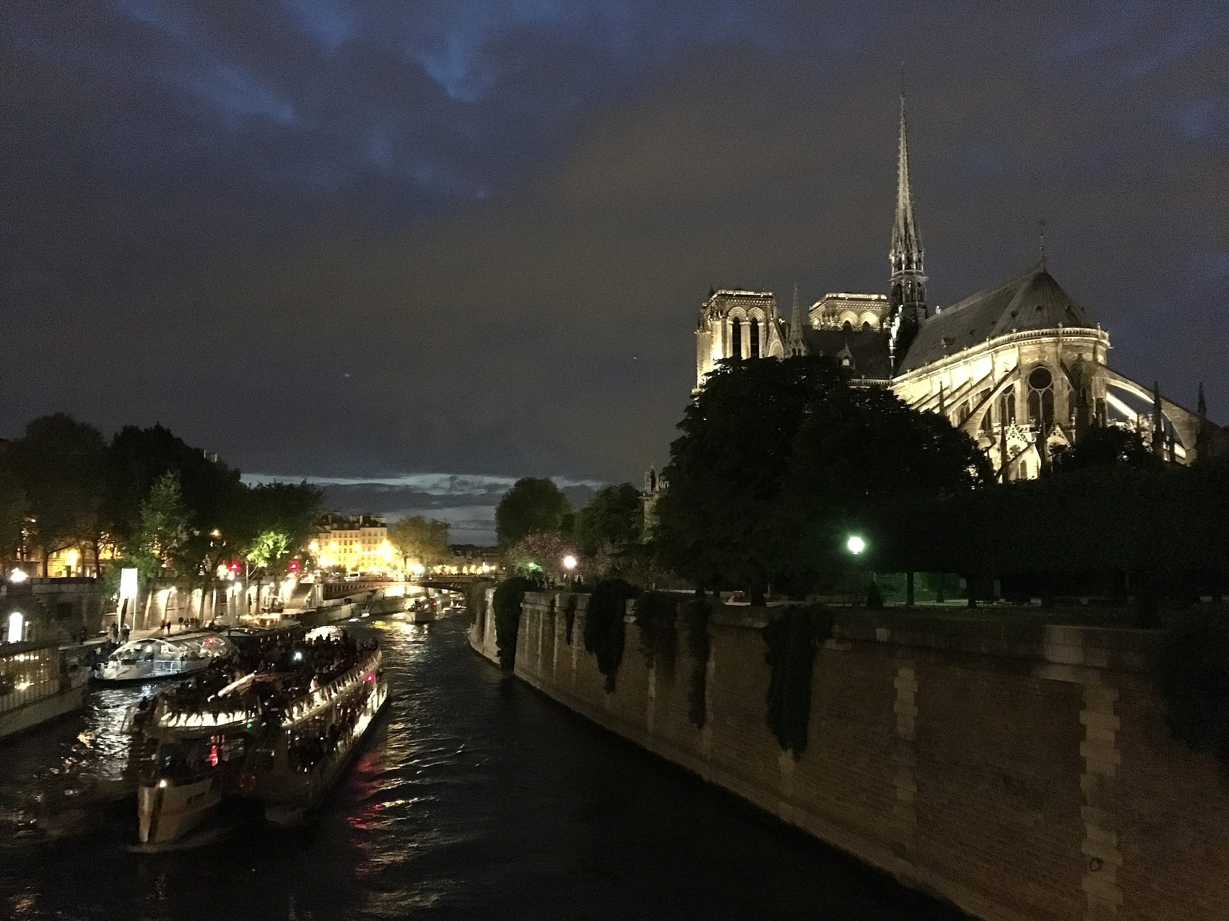 Notre Dame Cathedral light up at night from the river with a tour boat passing