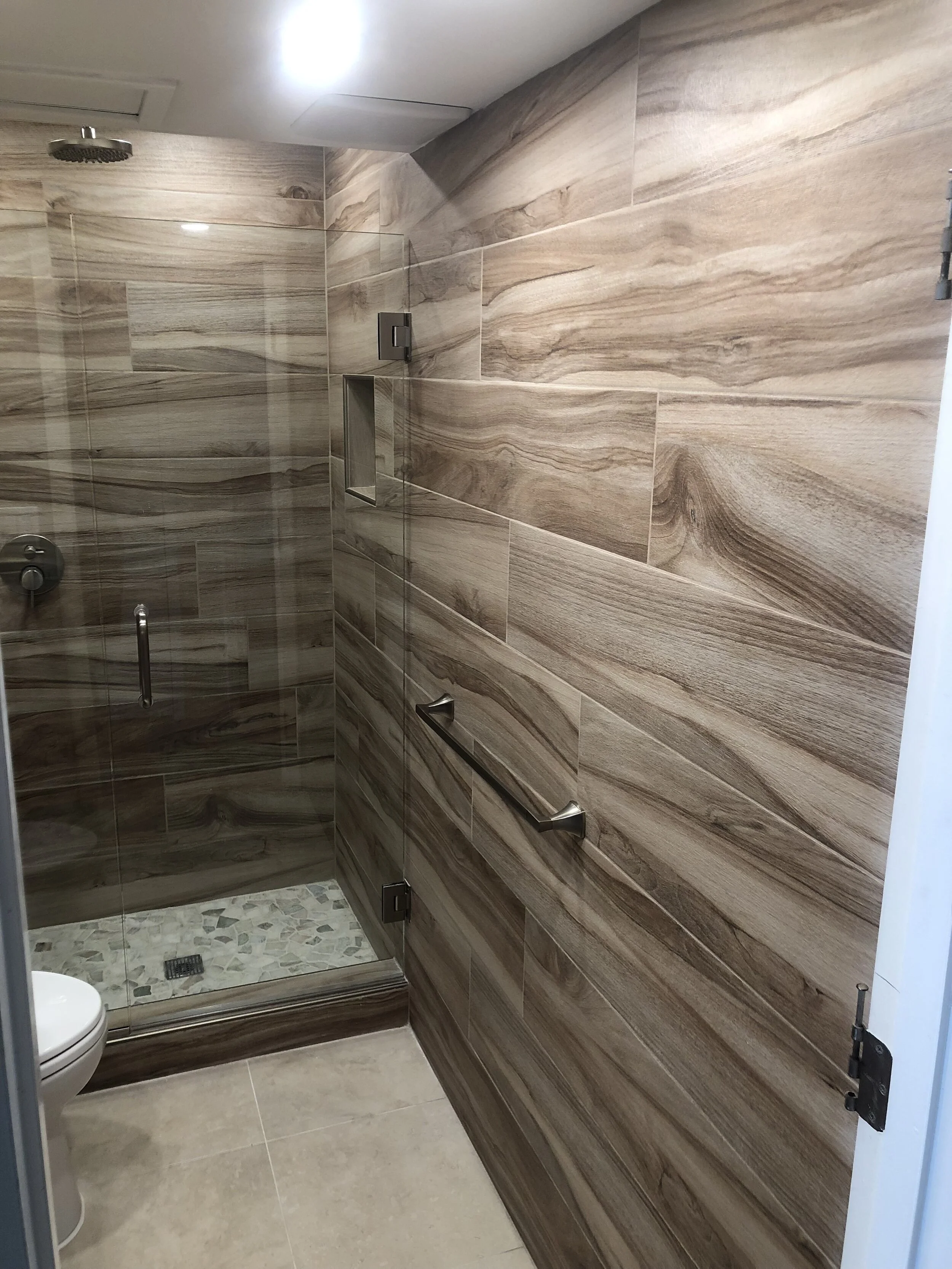 Bathroom with wooden-look tile on walls, a glass shower enclosure, and a toilet.