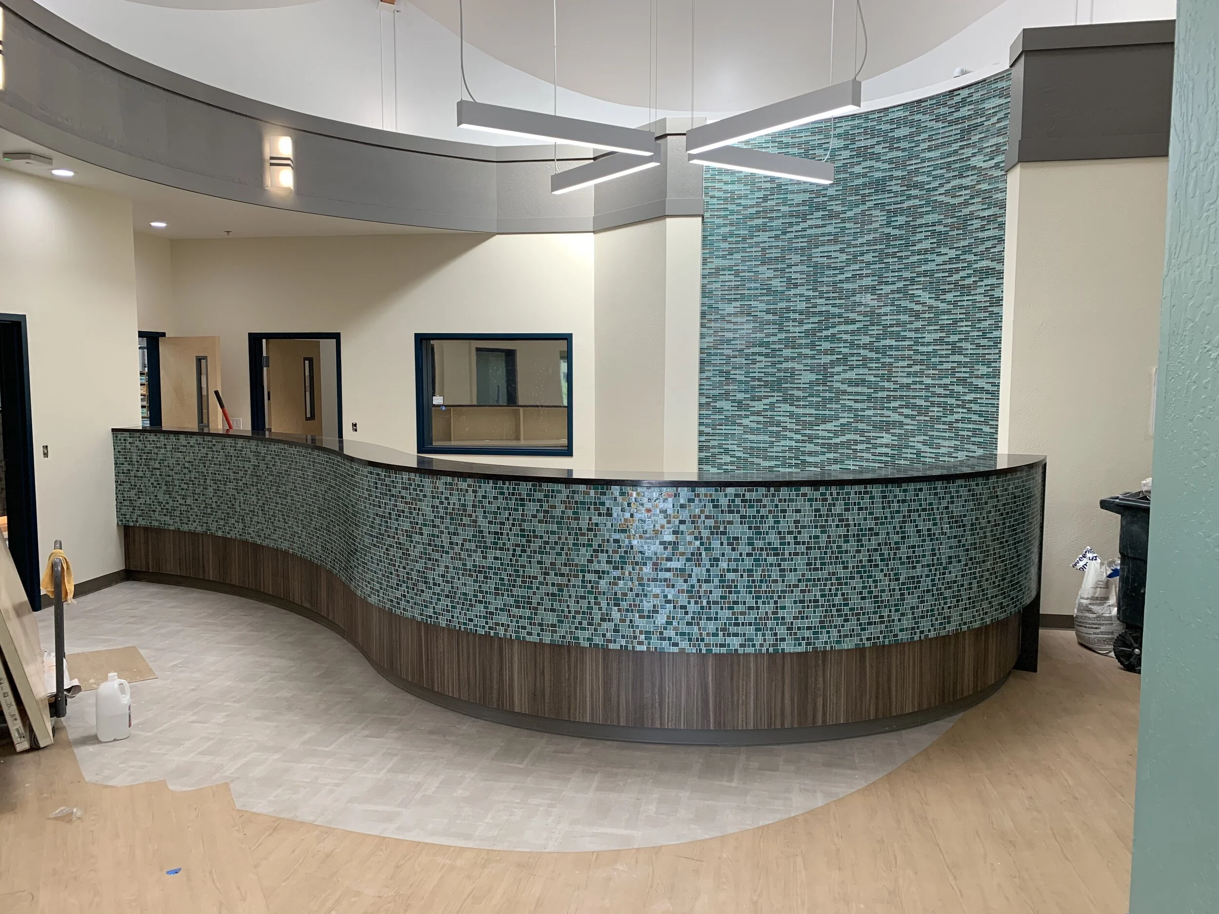 Interior view of a modern building with a curved mosaic tiled reception counter and glass windows, under construction or renovation.