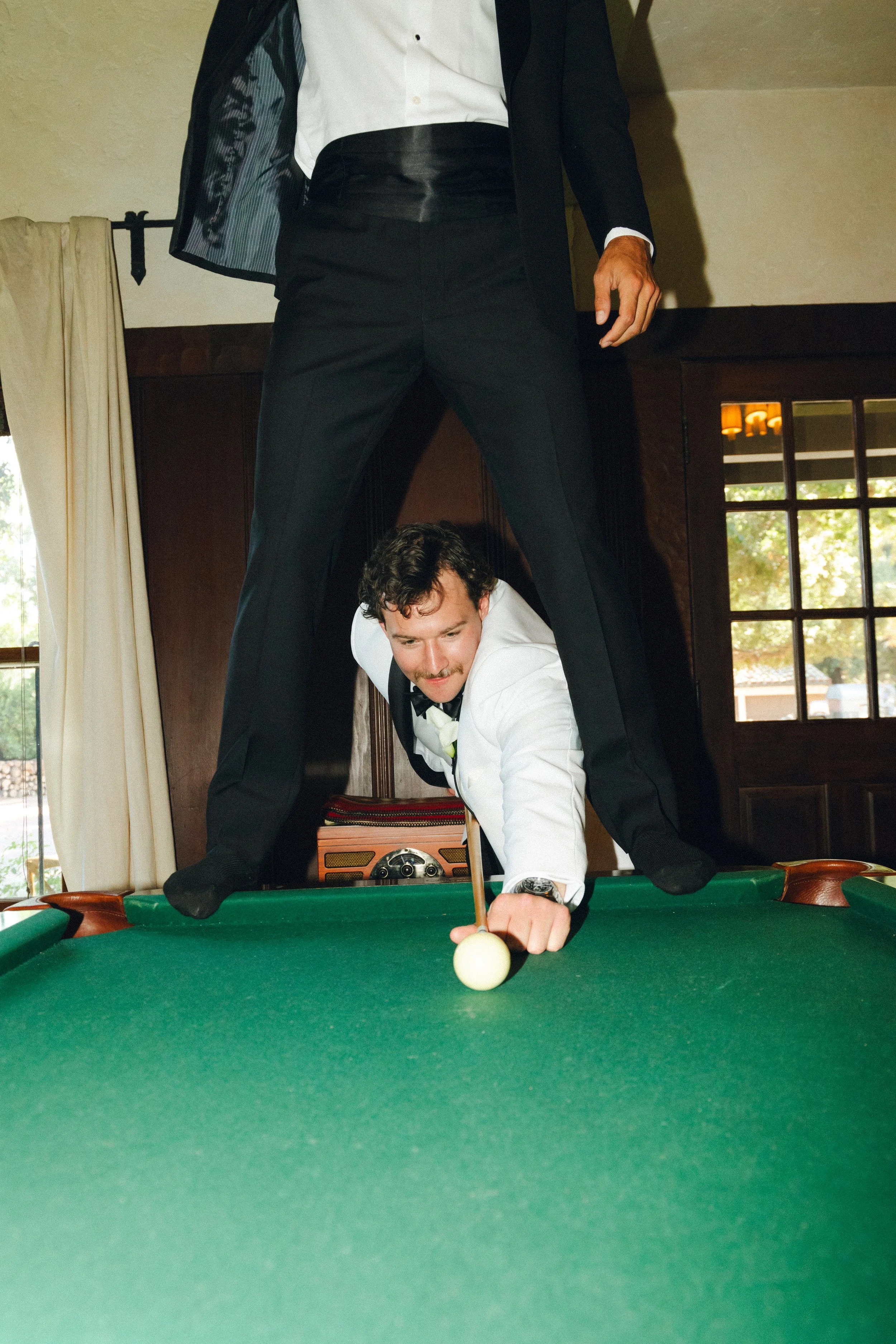 groom shooting pool on wedding day between groomsmen legs
