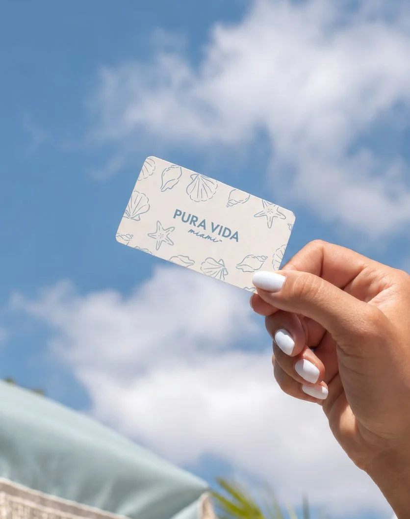 A hand holding a Pura Vida Miami gift card against the sky