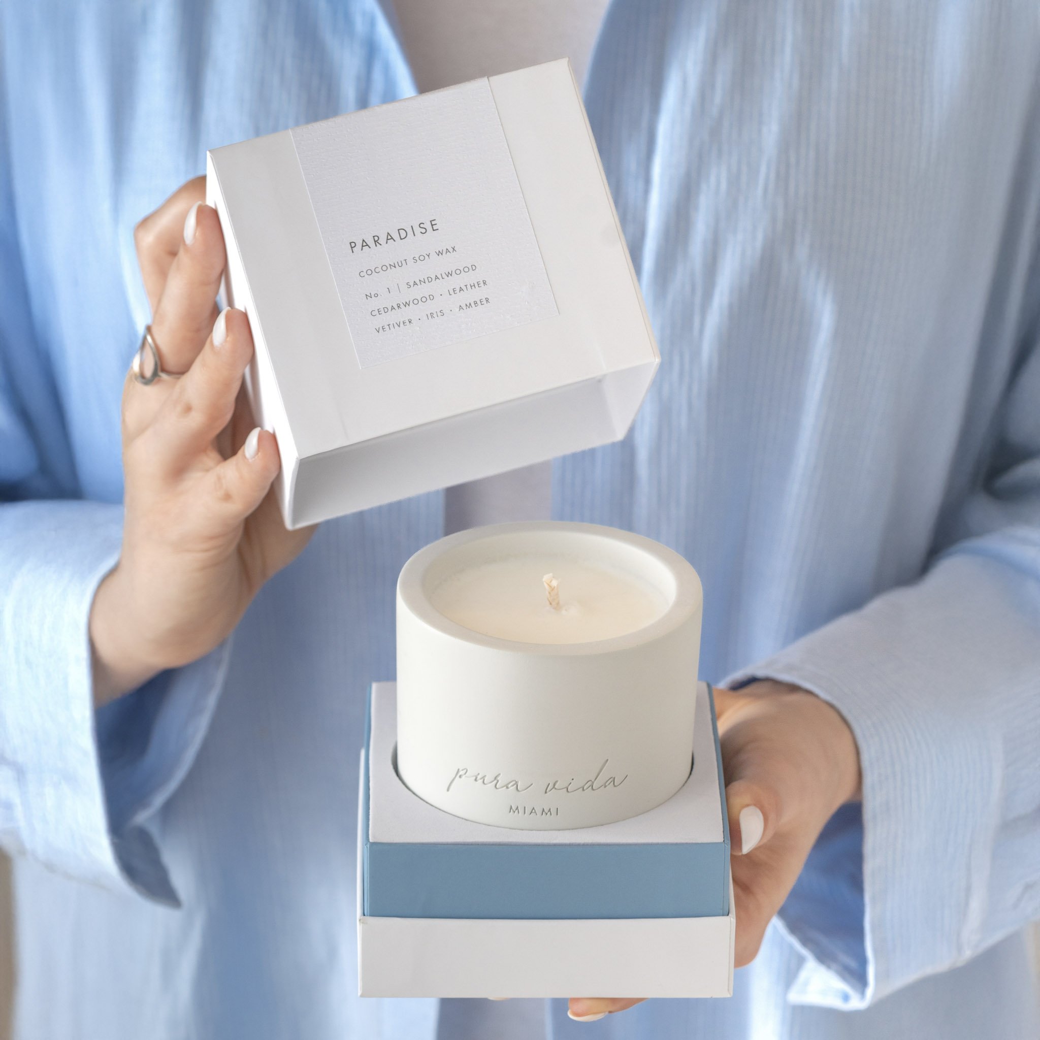 Women wearing a light blue button down shirt holding a Pura Vida Miami candle box 