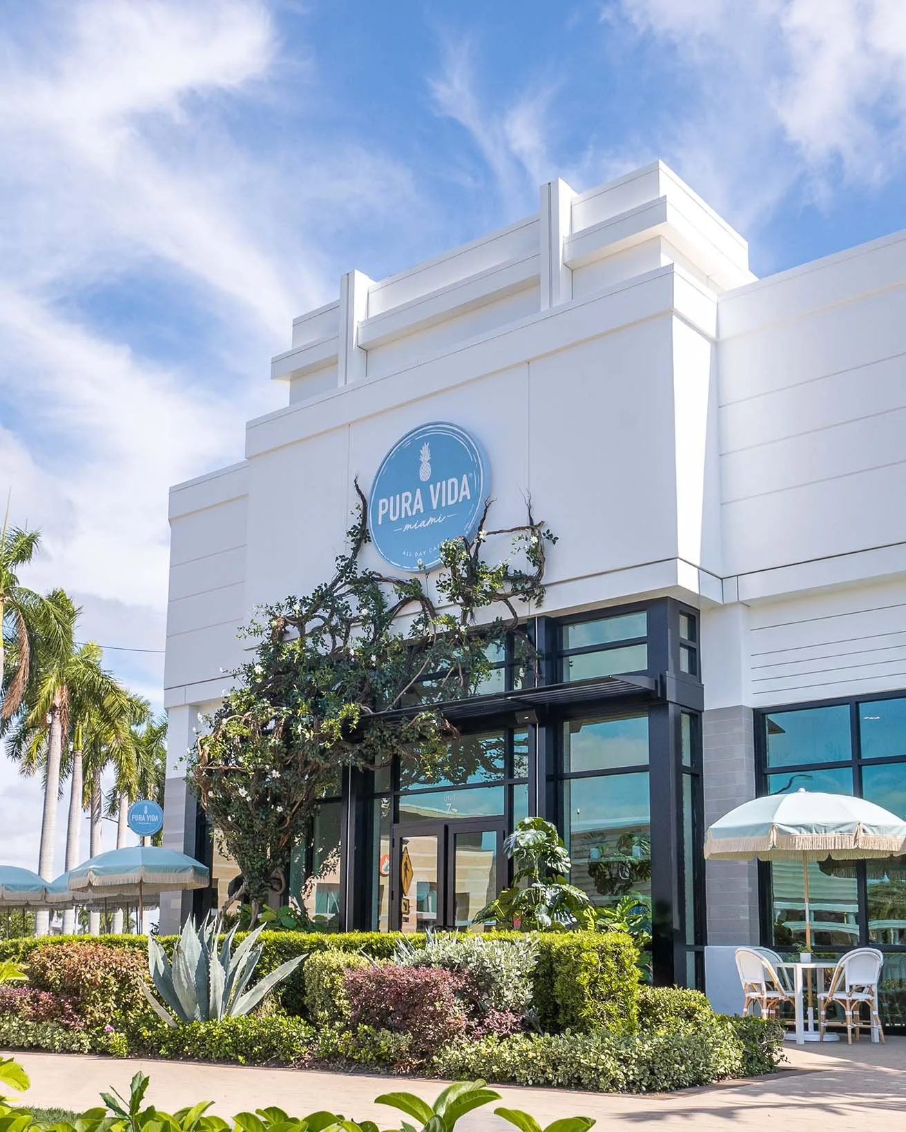 Pura Vida Miami café exterior with plants and outdoor seating under blue skies.