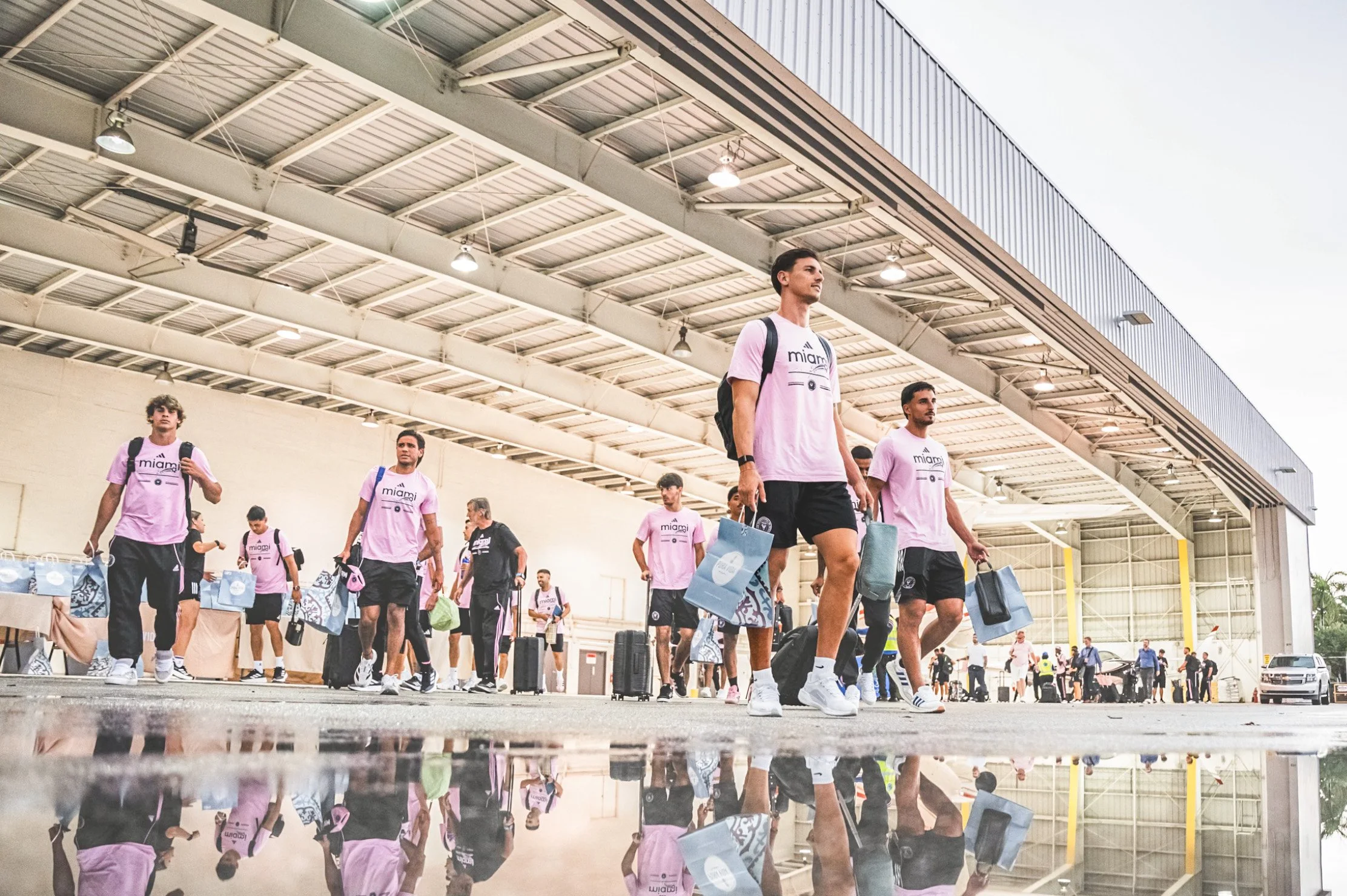 Group of young men in pink t-shirts carrying luggage and bags at an airport or transportation terminal