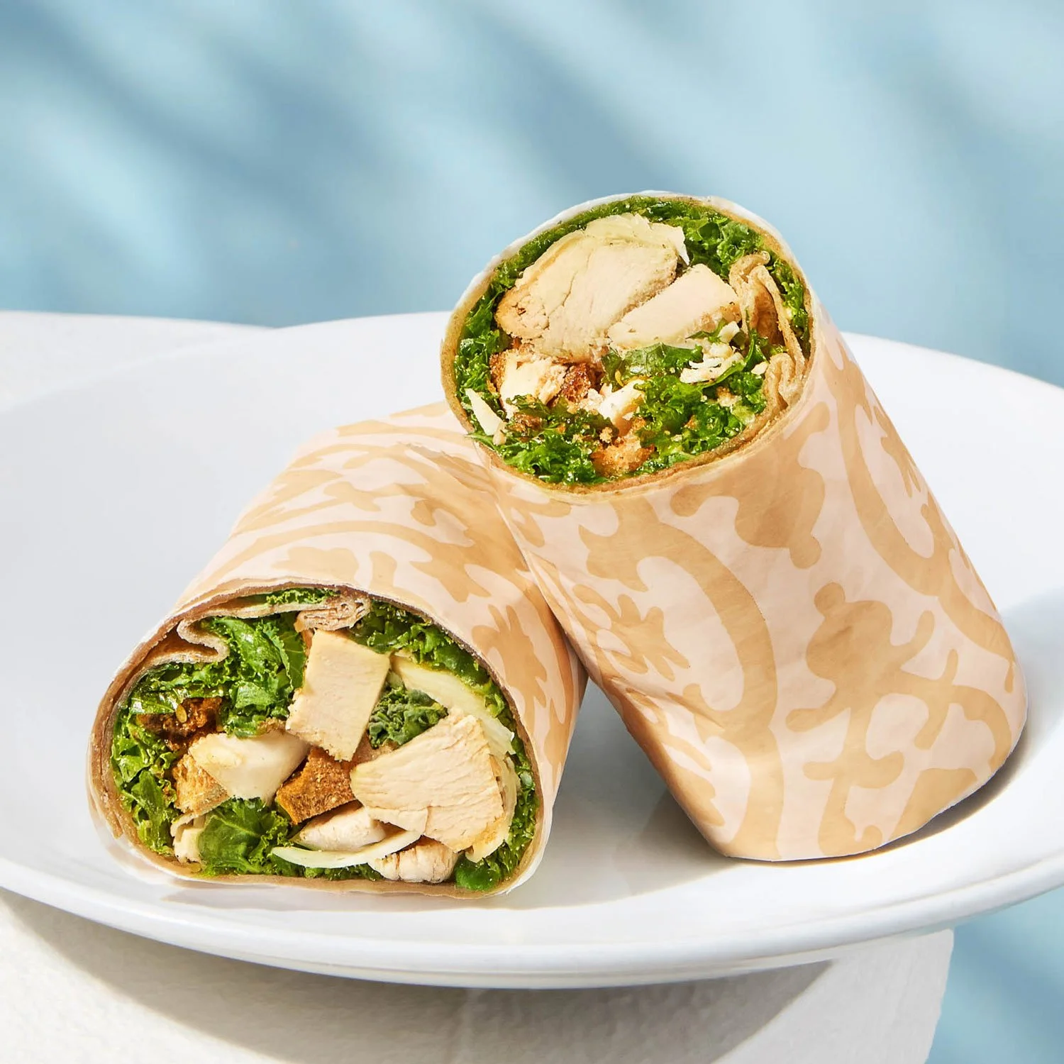 Close-up of chicken Caesar wrap cut in half, filled with grilled chicken, lettuce, and Caesar dressing, on a white plate with a side of waffle fries