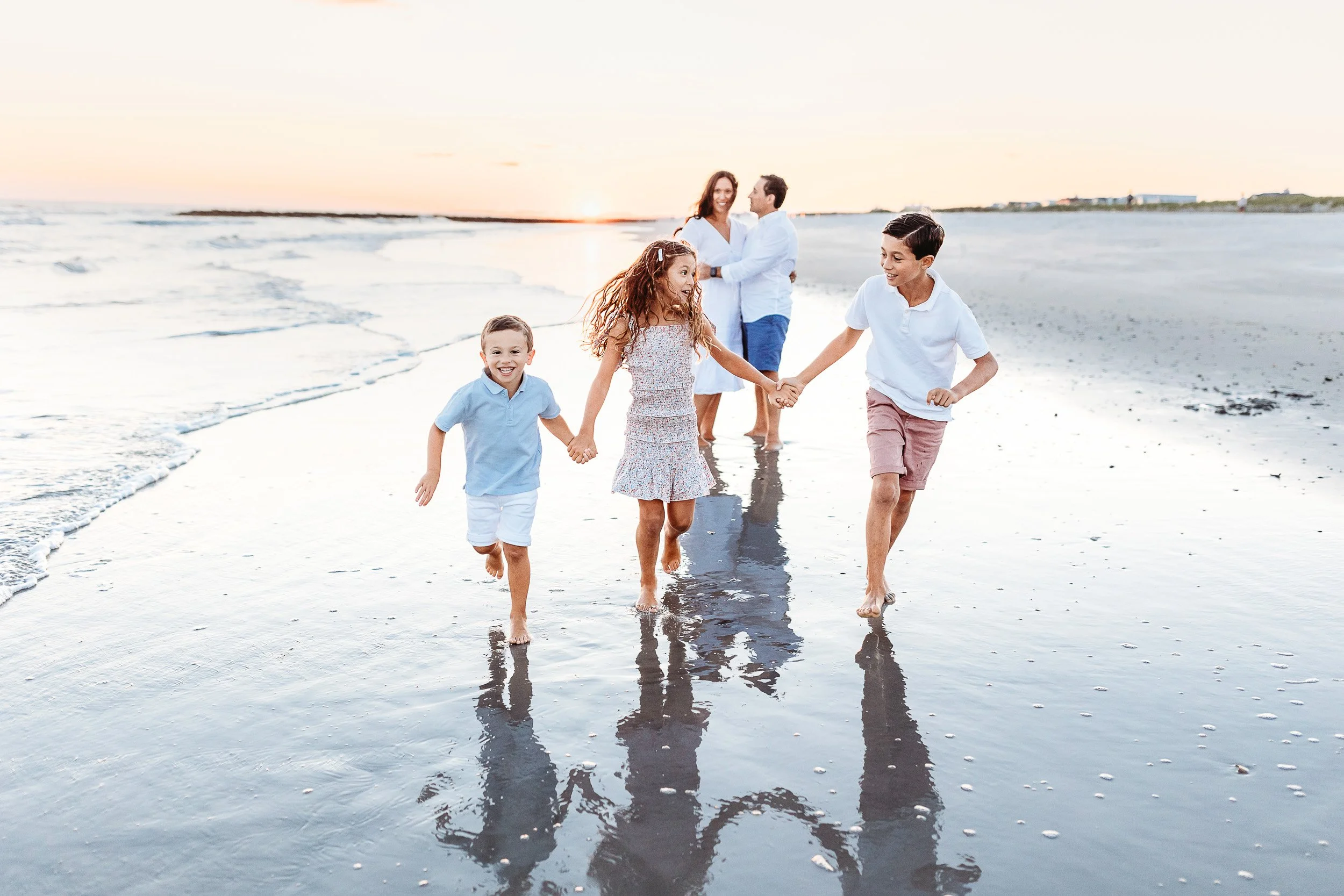 kids running hand in hand on the beach at sunset and laughing while parents watch