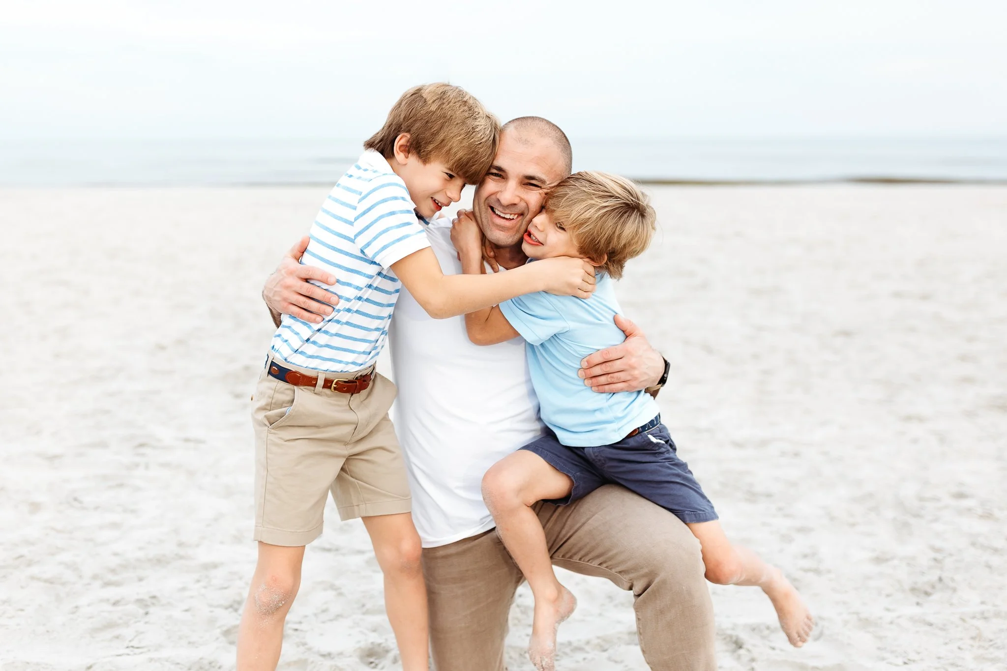 dad embracing and laughing with his sons on the beach during a family session