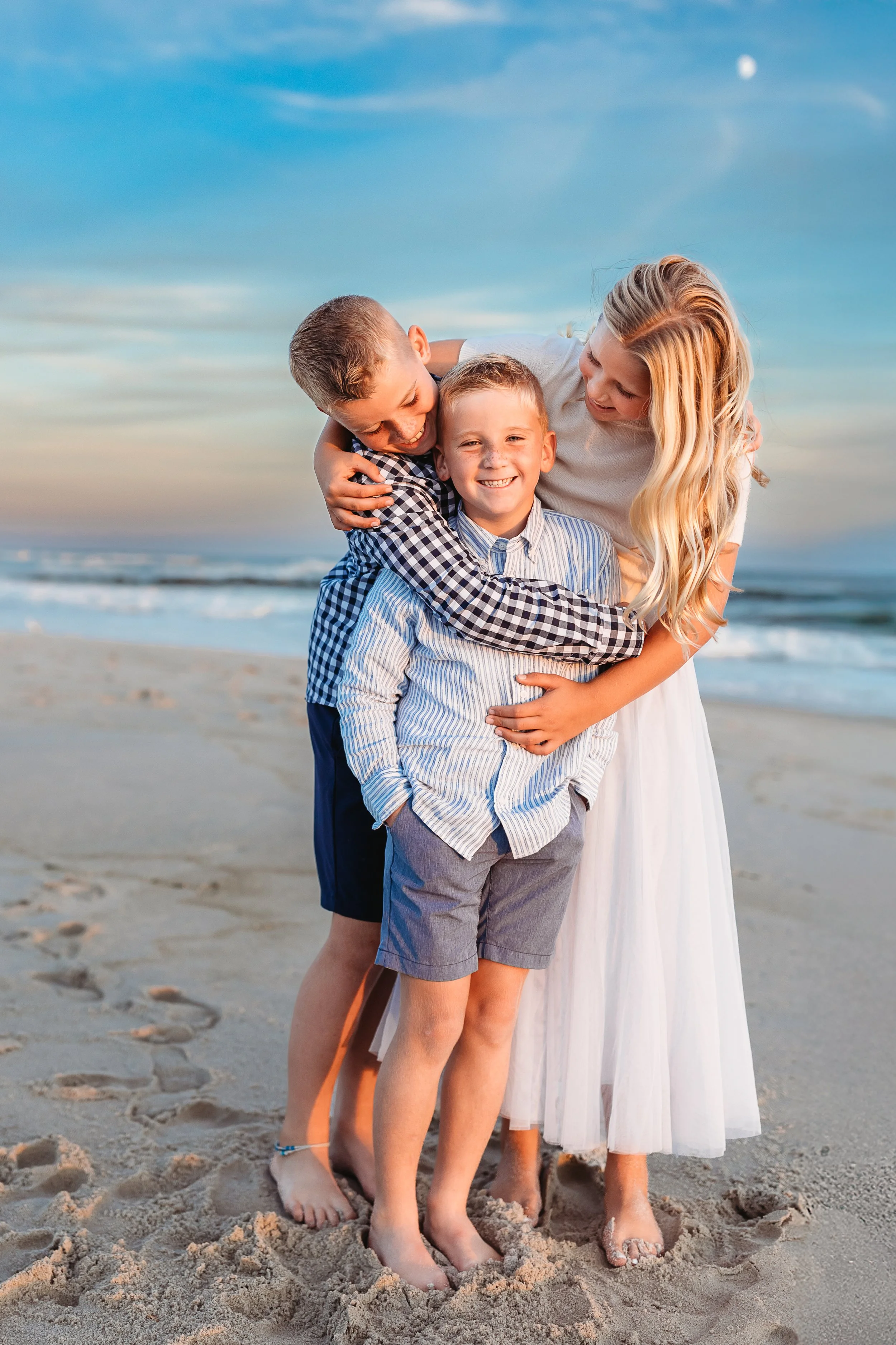 siblings on Atlantic beac at sunset embraced and their is a pink and blue sunset sky and the moon is in the horizon