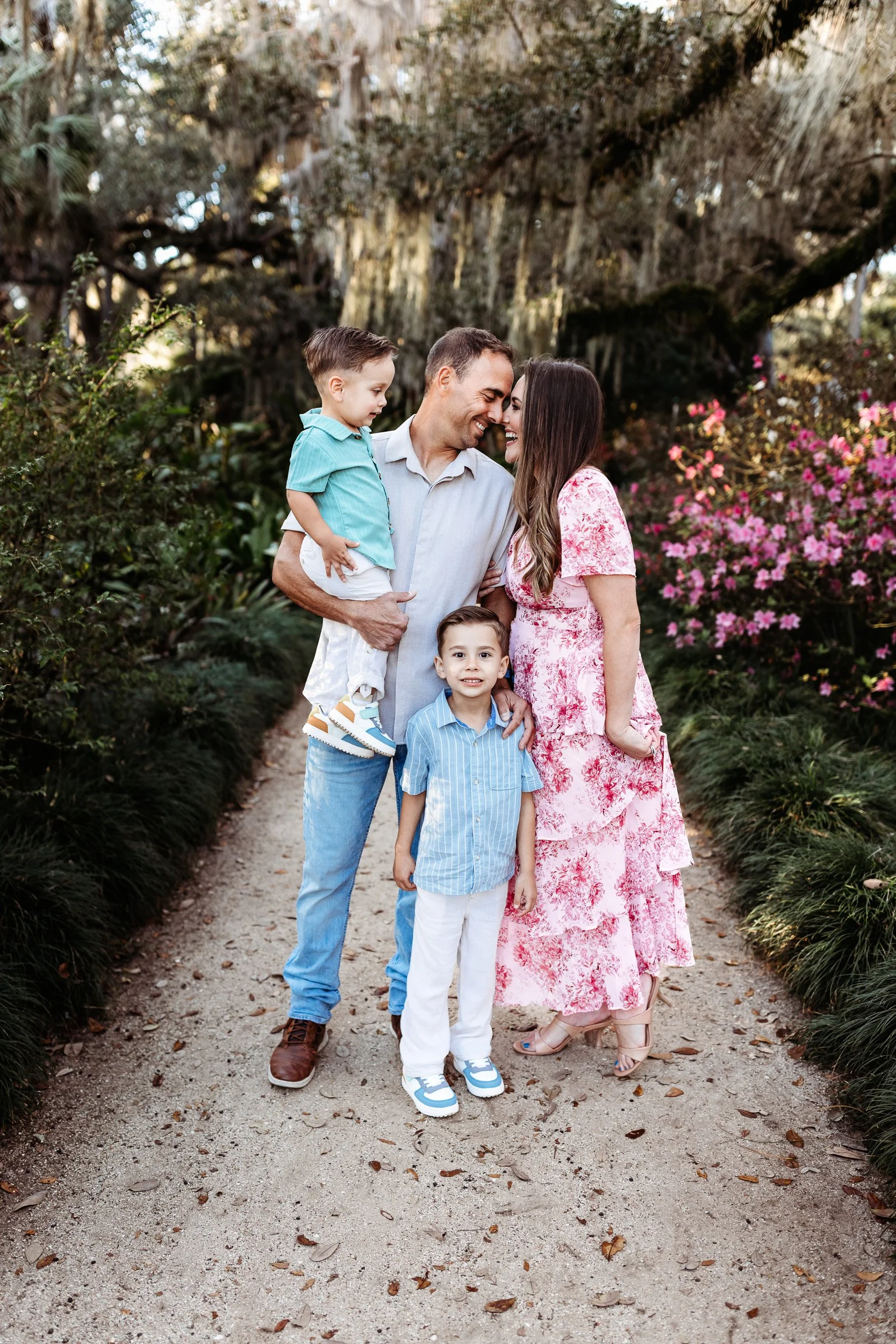 family on a path at a garden and the mom and dad are leaning in head to head and laughing
