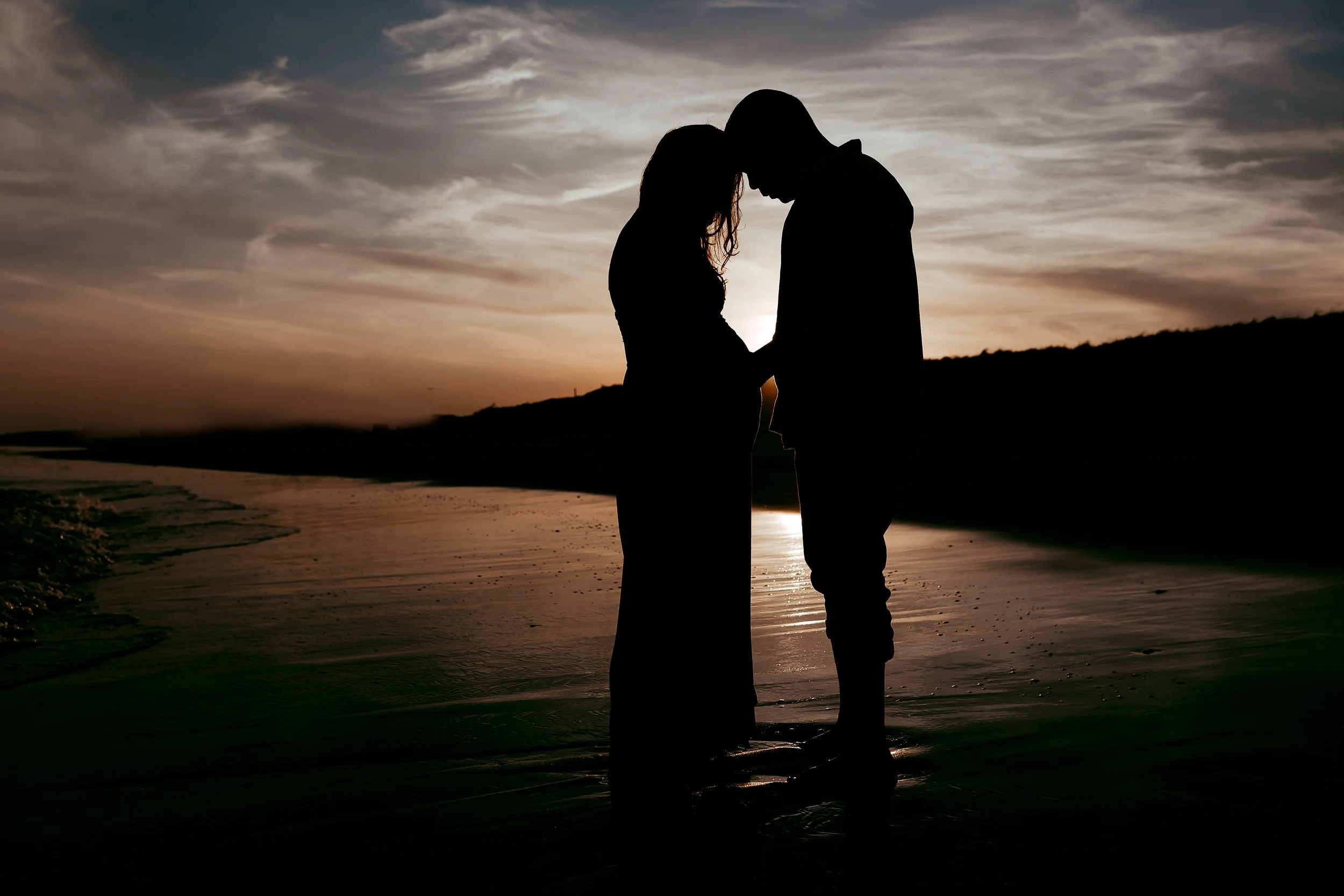 silhouette of a couple at sunset on Neptune Beach  and they are looking at the woman's pregnant belly