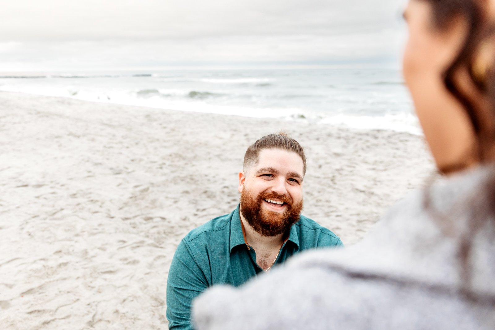 man on knee proposing to woman on a beach and smiling