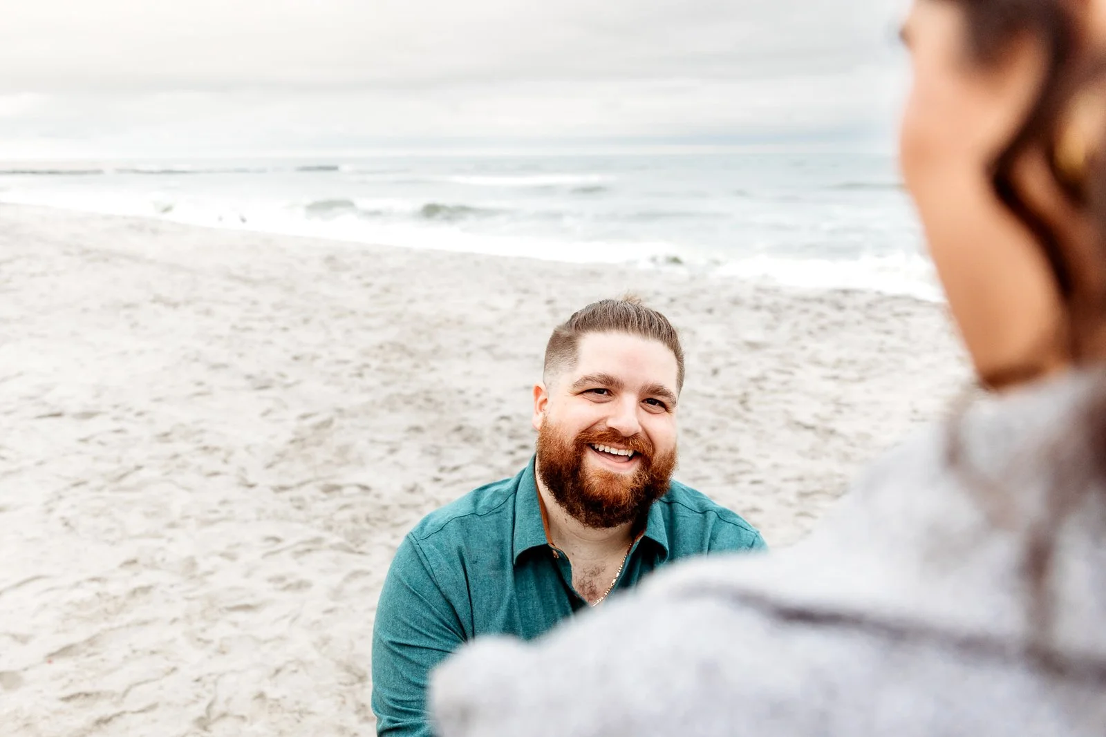 man on knee proposing to woman on a beach and smiling