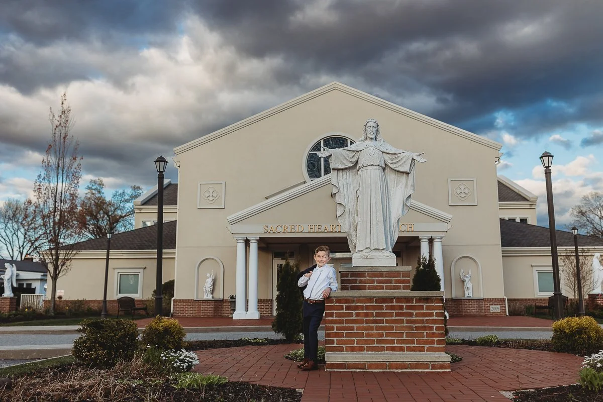 boy standing in front of a church on communion day leaning on statue pedestal