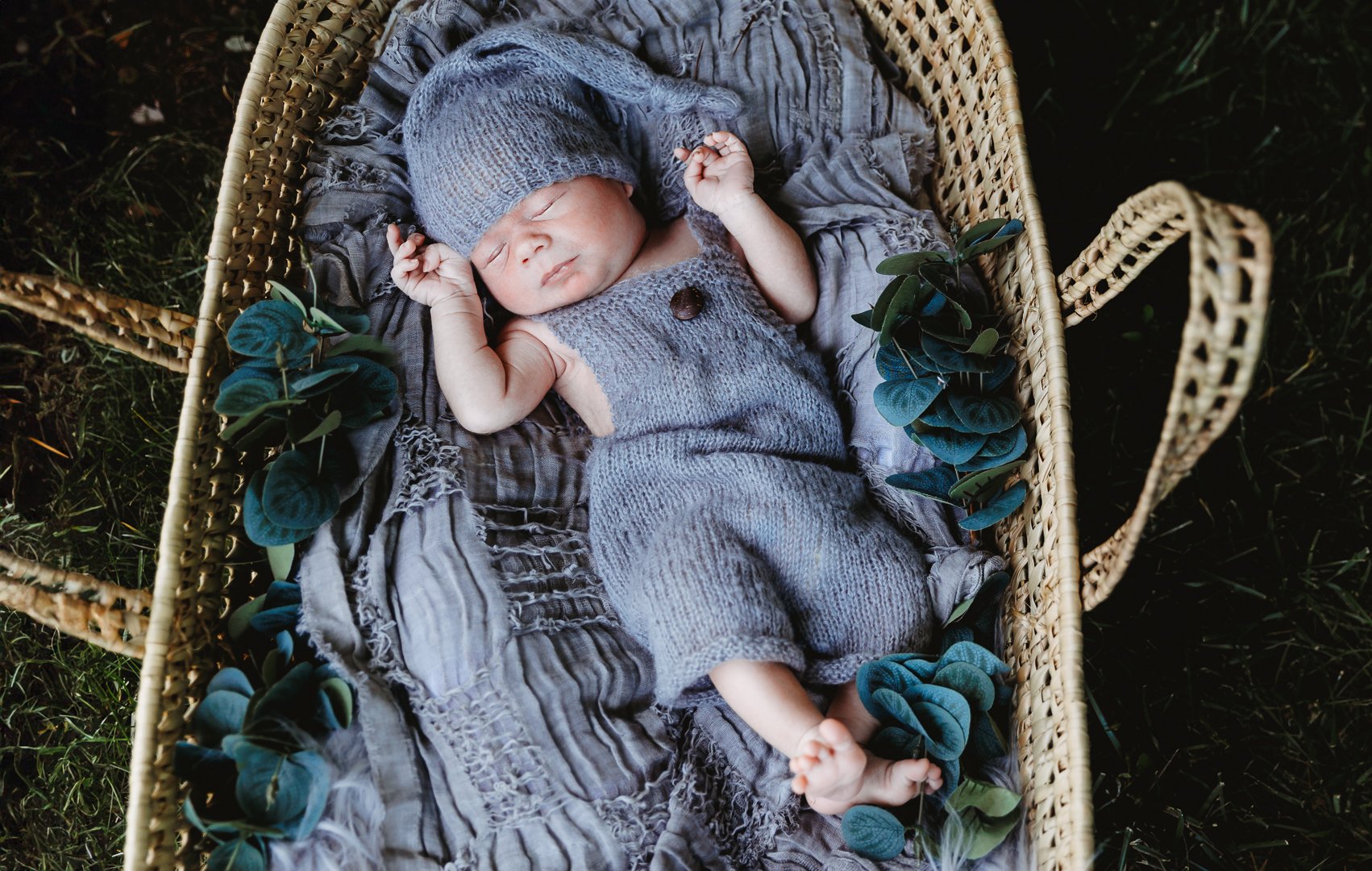 baby sleeping in moses basket in grey romper and knit hat