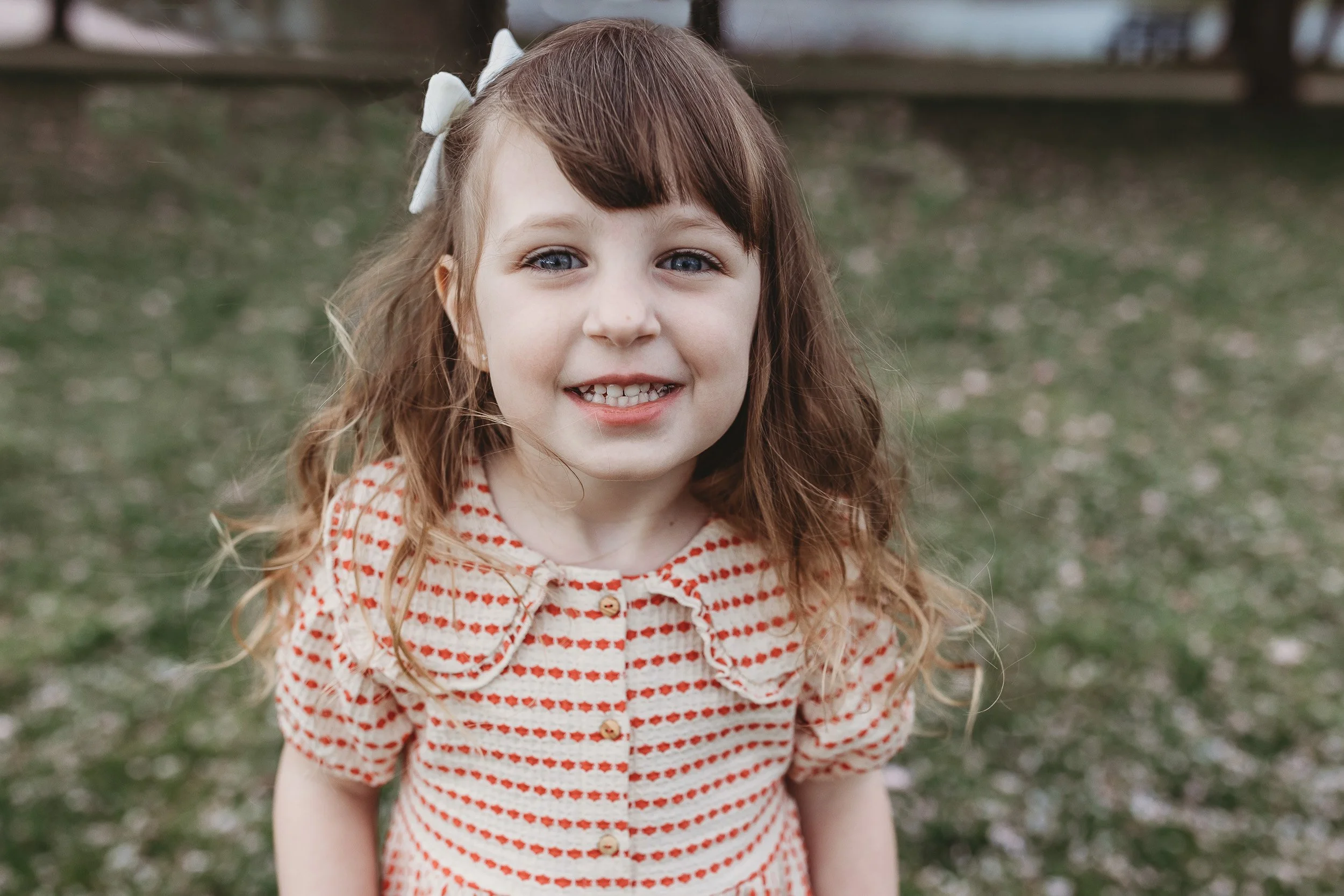 close up of a toddler girl for spring family portraits in Jacksonville and she is wearing a red and cream color vintage dress