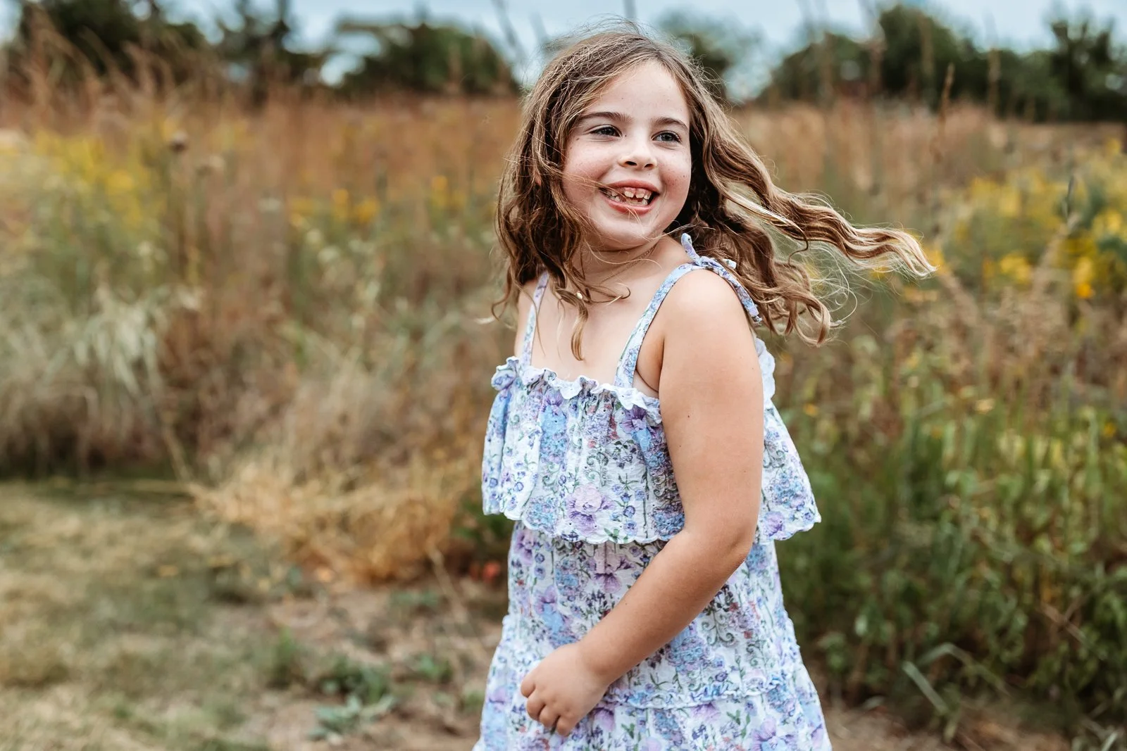toddler in a field in st augustine for birthday photos and her hair is blowing in the wind while she laughs