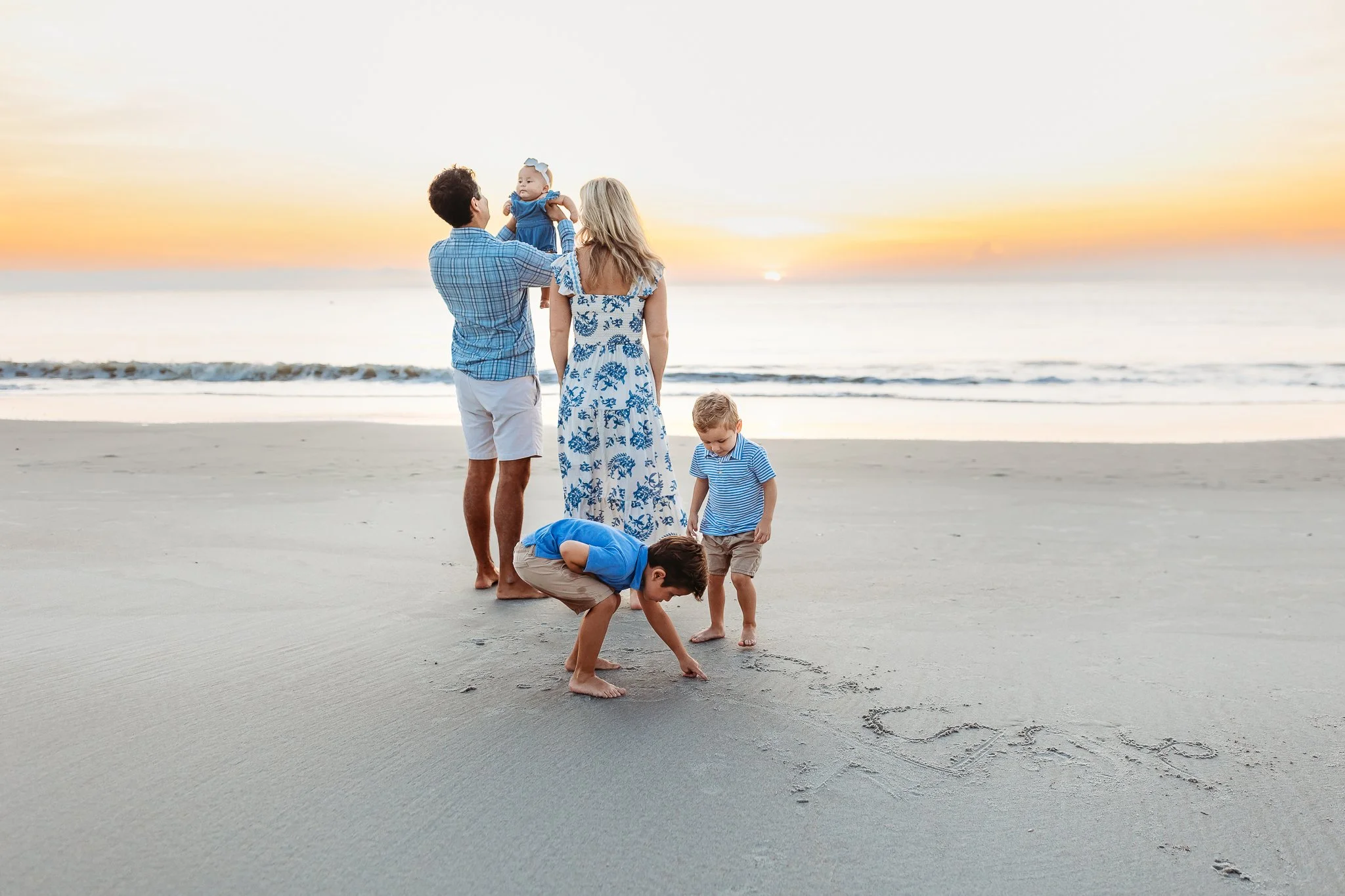 storytelling image of a family on the beach at sunrise boys are writing in the sands parents holding a baby
