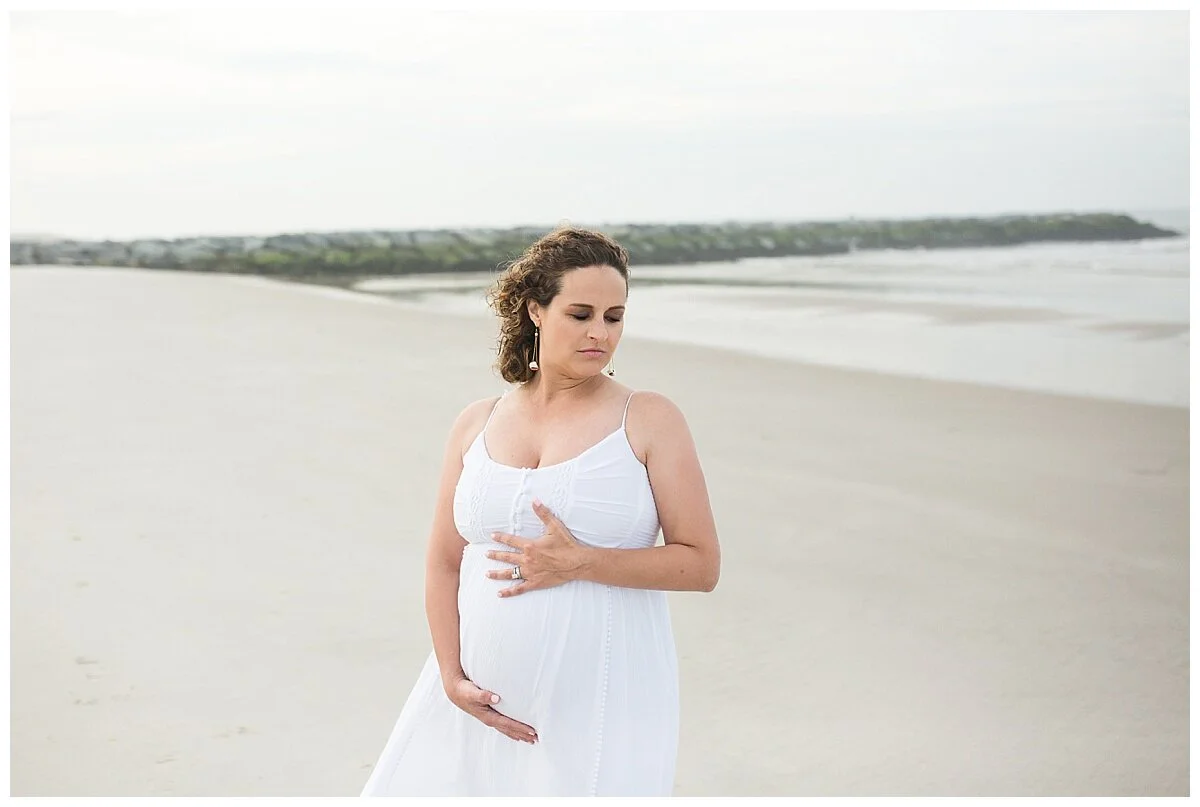 natural outdoor maternity photo at the beach with a jetty in the background and mom in white crisp linen dress