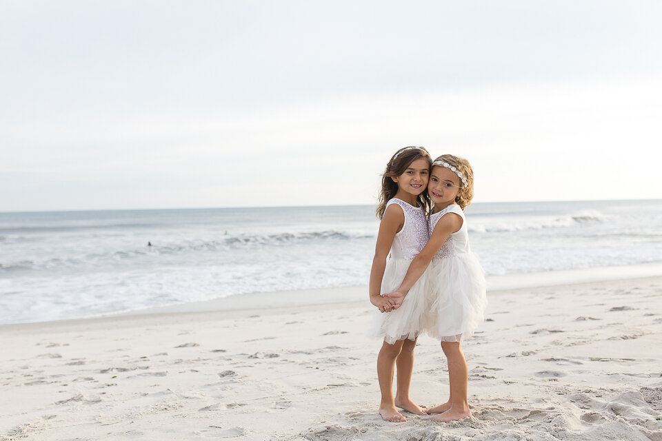 sisters in white dresses on the beach holding hands