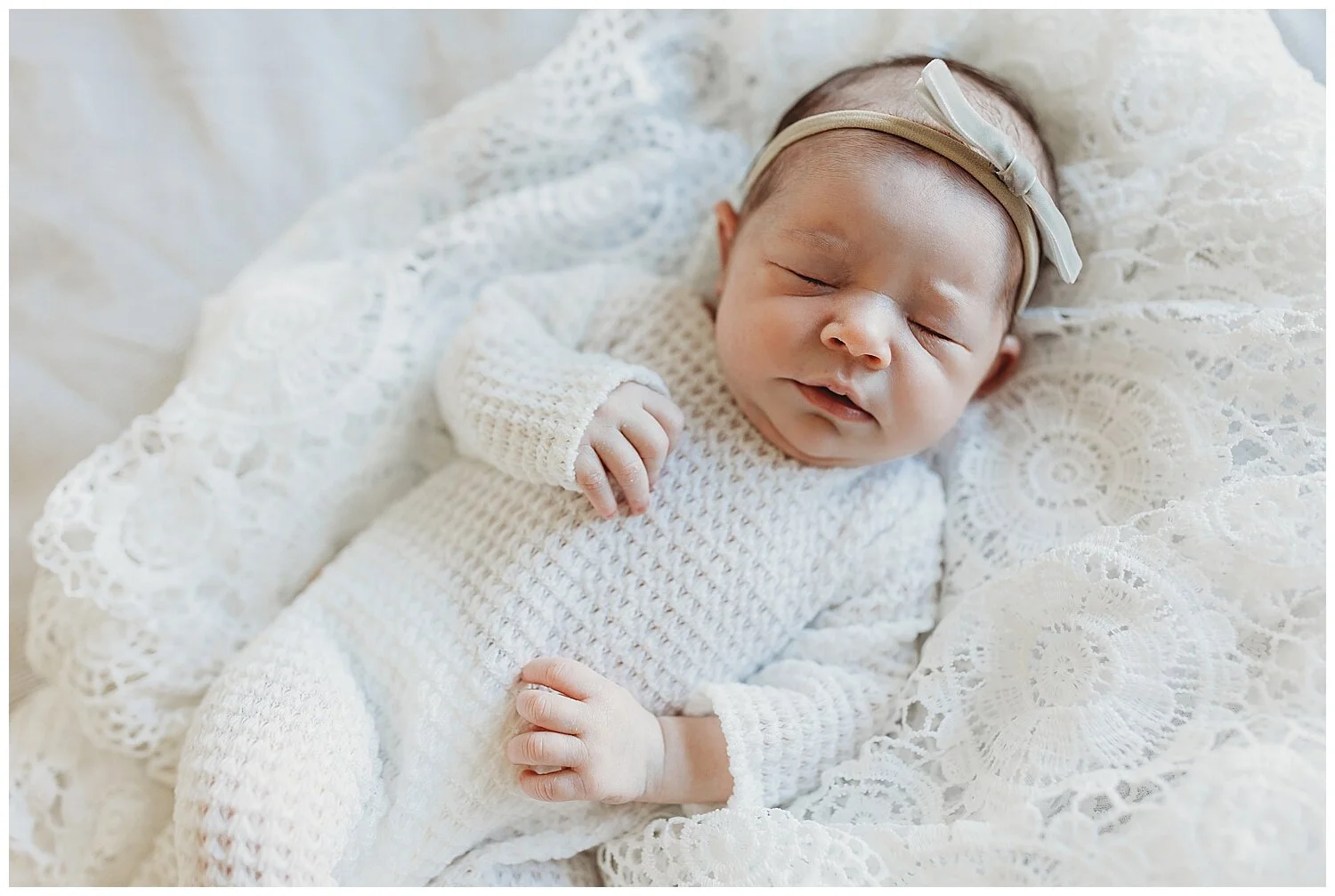 baby in white jumper and grey headband sleeping on white lace crochet blanket
