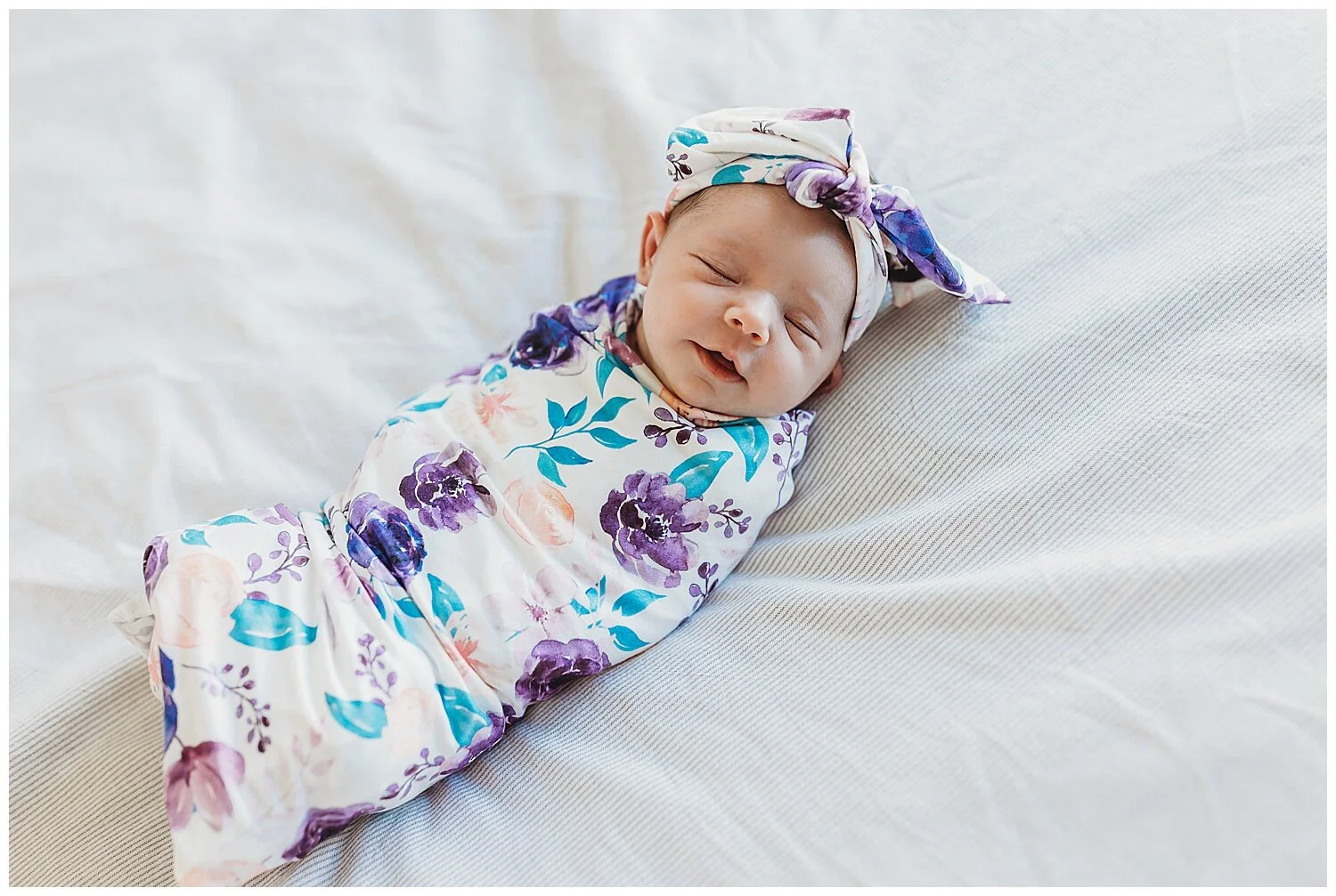 baby swaddled in pink and purple floral wrap sleeping with a soft smile on her face